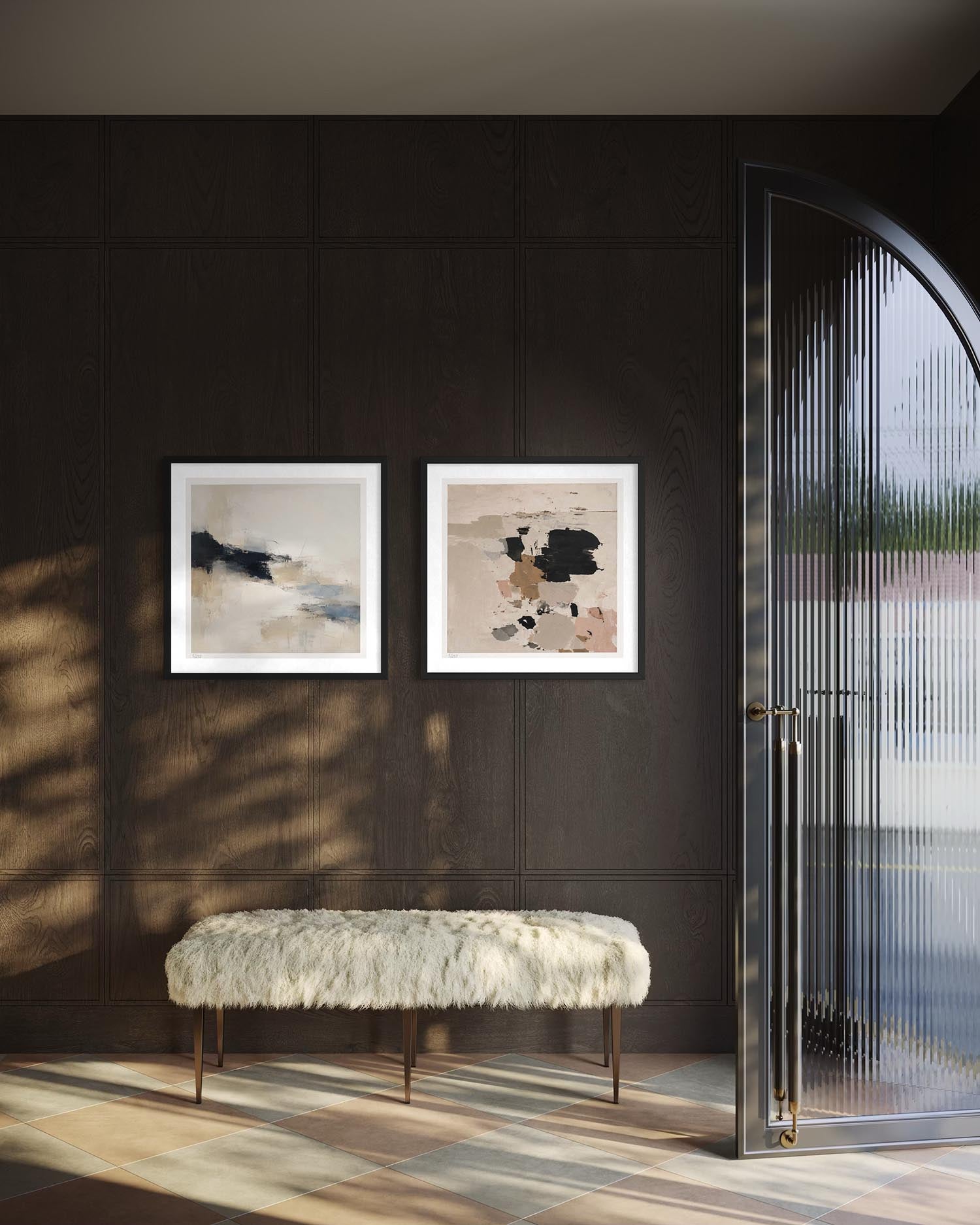 Two framed abstract art prints with white frames hang on a dark wood-paneled wall above a white faux-fur bench. A glass arched door is visible on the right, with warm sunlight casting shadows across the floor.