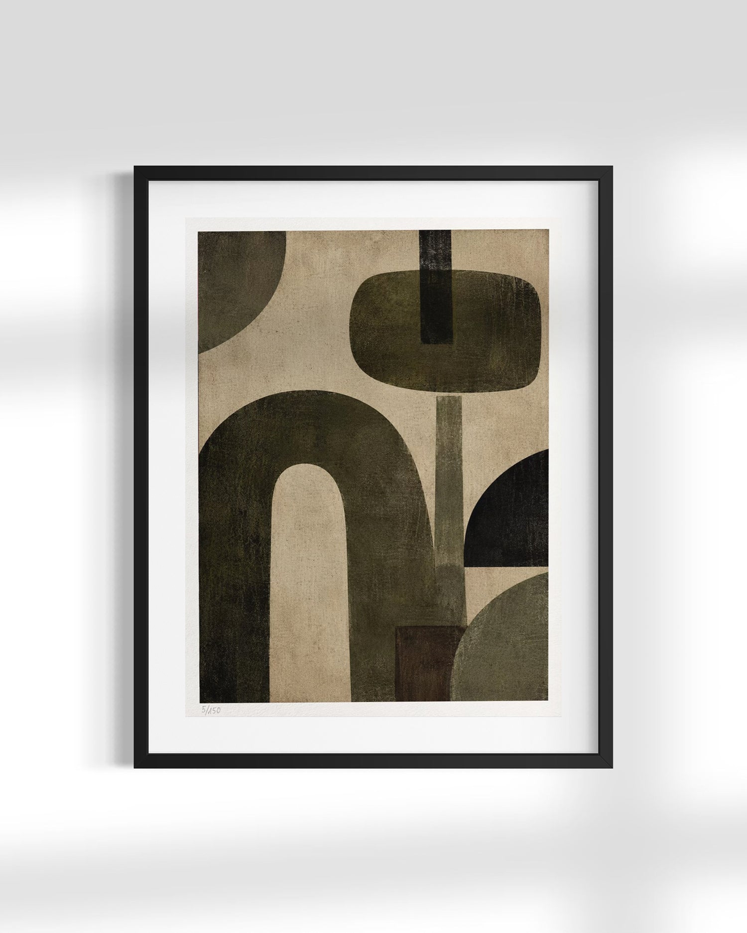 A framed abstract art print featuring organic shapes in dark olive green, black, and beige on a white mat and black frame, displayed against a light gray wall with soft shadows.