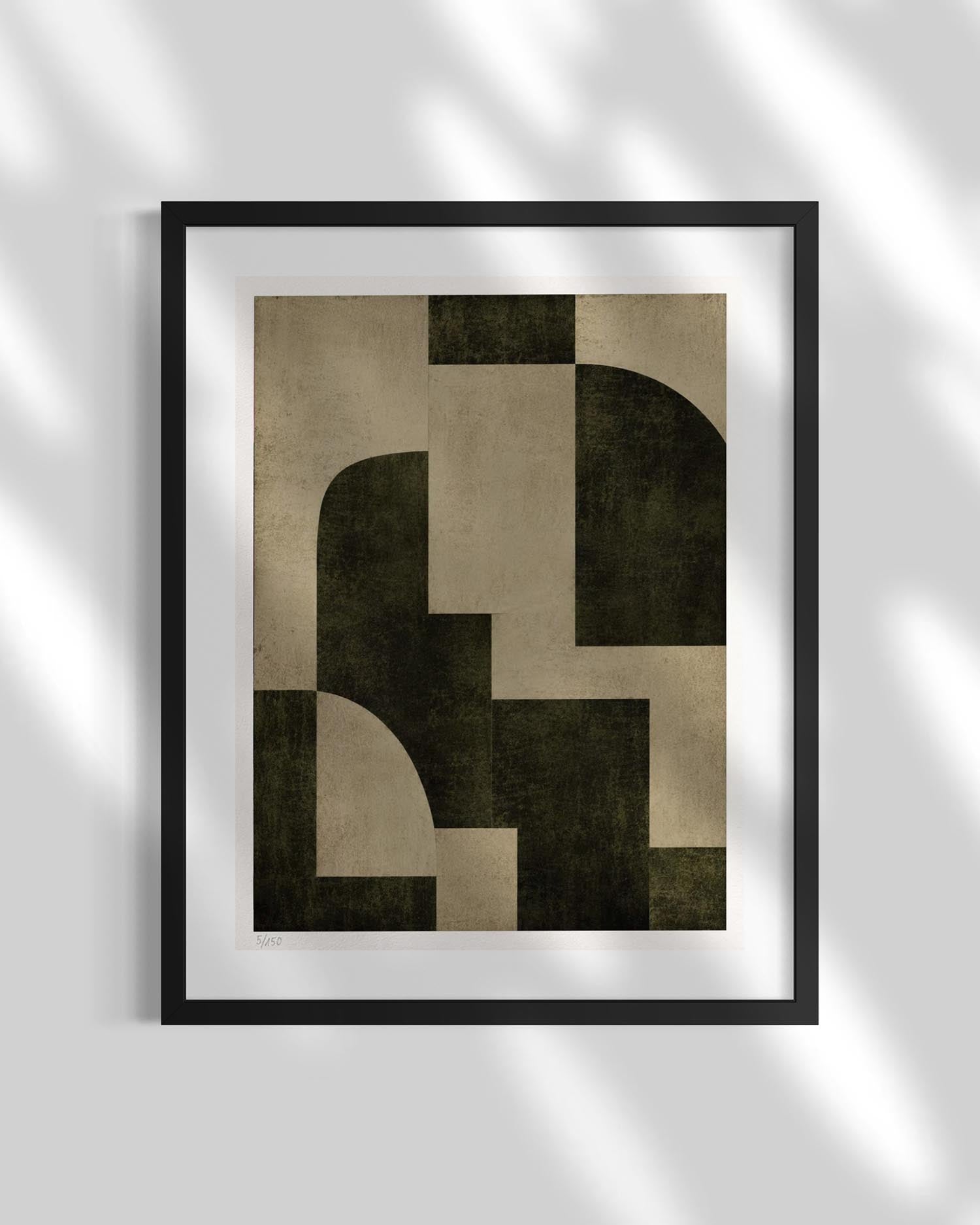 A framed abstract geometric art print with dark olive green and beige shapes, displayed on a light gray wall with soft leaf shadows.