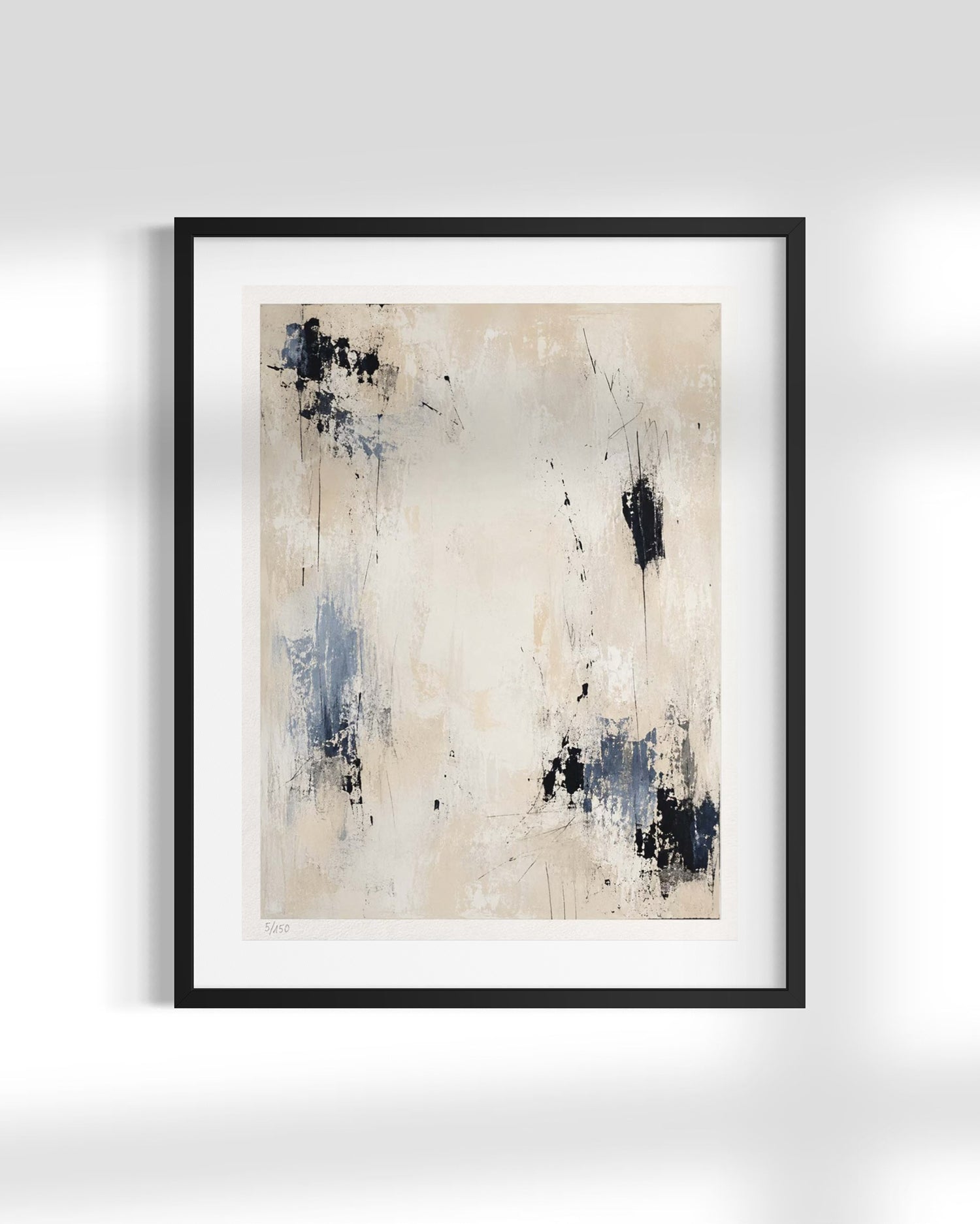 Framed abstract wall art featuring a minimalist beige background with textured blue and black paint splatters, presented in a black frame with a white mat against a light gray wall.