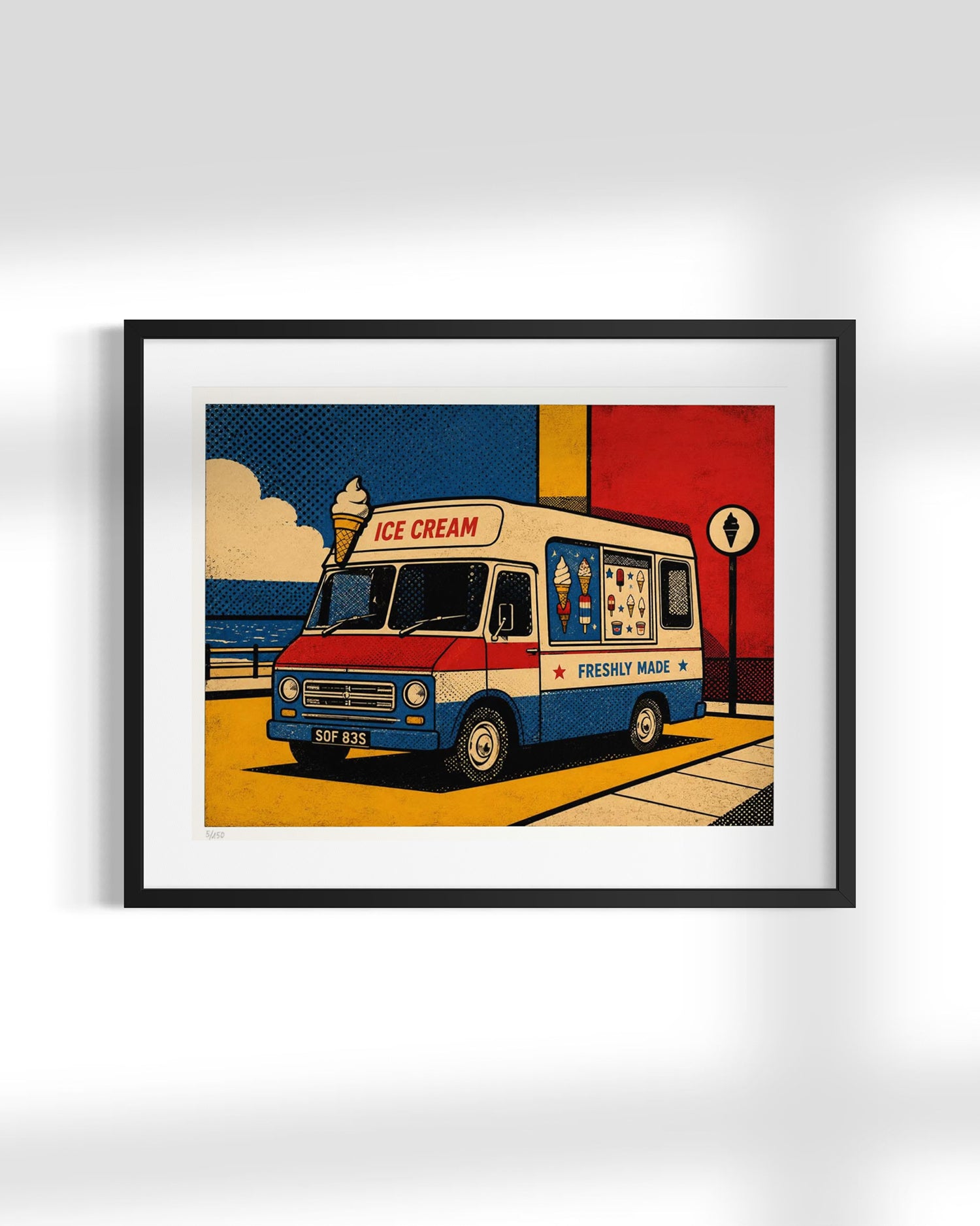 Framed pop-art style ice cream truck print hanging on a light gray wall. The artwork shows a cream, red, and blue ice cream van with the words 'ICE CREAM' and 'FRESHLY MADE' on a yellow street scene with a blue sky and red building background.