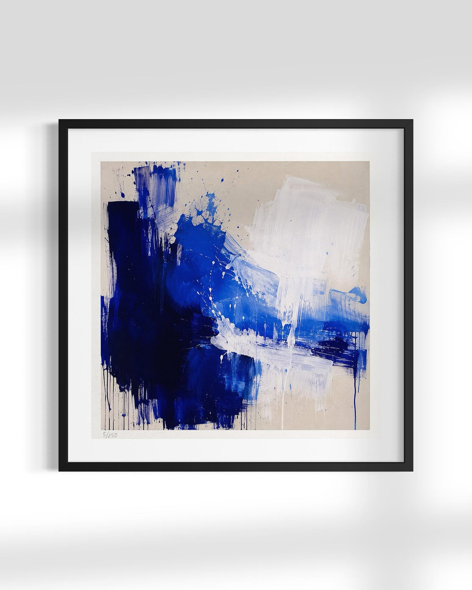 Framed abstract wall art featuring bold blue and white paint strokes on a warm beige background, presented in a black frame with a white mat against a light gray wall.