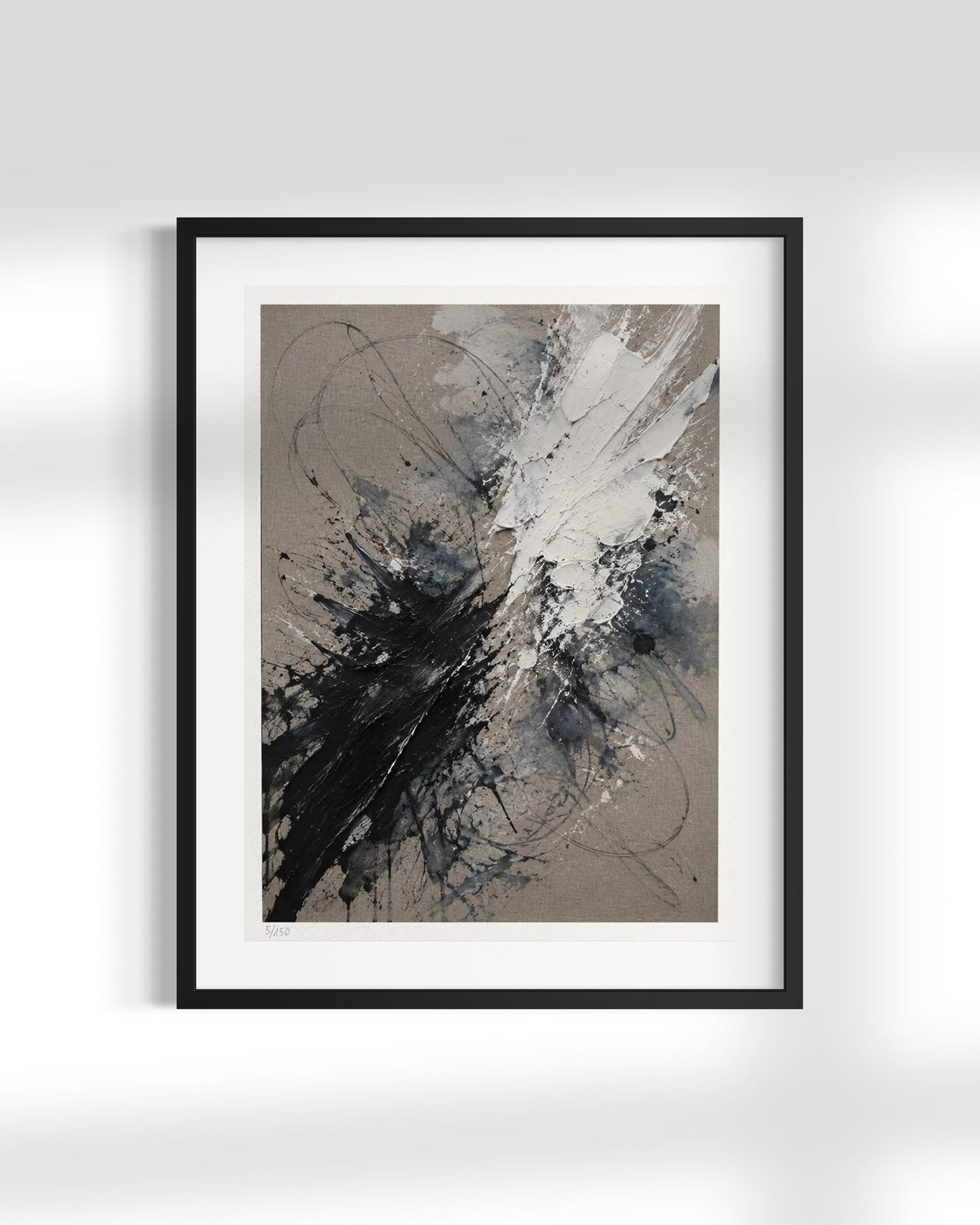A framed abstract art print featuring black, gray, white, and beige paint splatters, presented in a black frame with a white mat against a light gray wall.