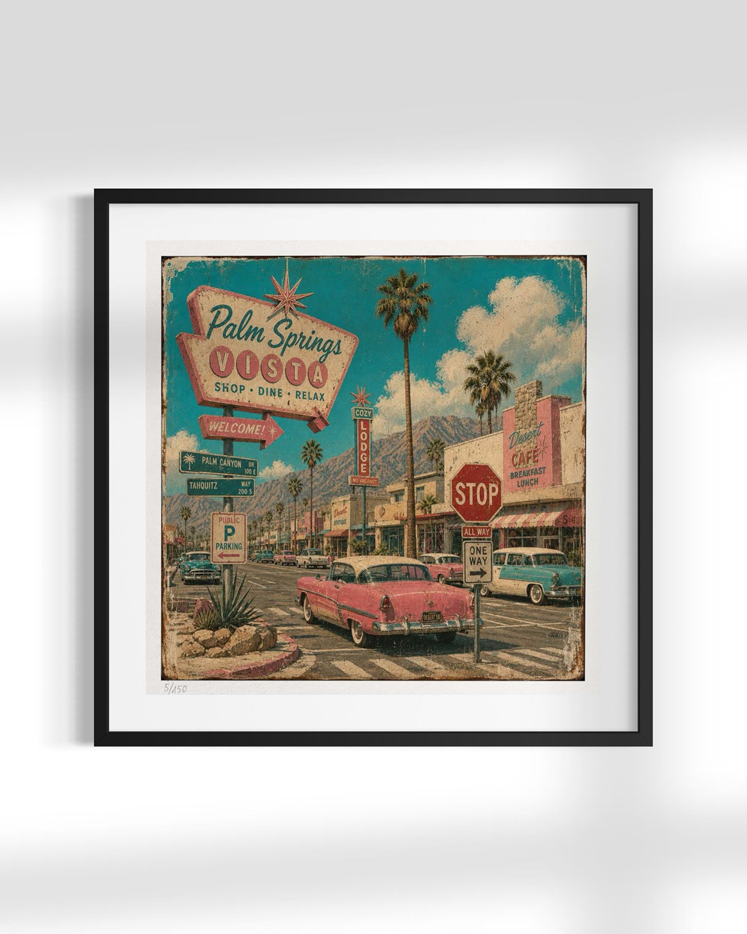 Framed wall art featuring a retro 1950s Palm Springs street scene with a pink car, palm trees, mountains, and signage, shown in a black frame with white mat against a light gray background.