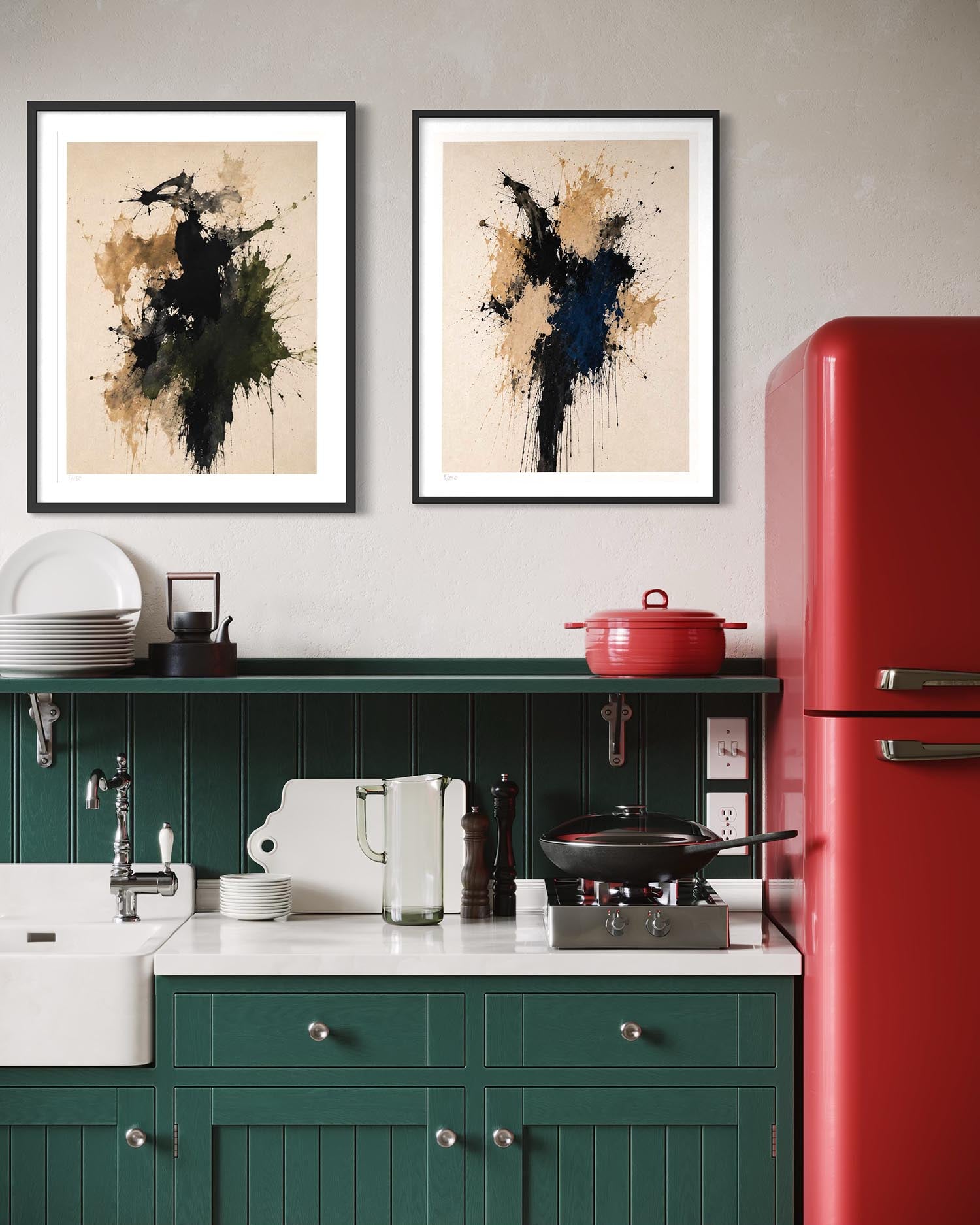 A styled kitchen interior featuring two framed abstract art prints hanging on a light gray wall above a dark green cabinet and white countertop. A red refrigerator is visible on the right, along with kitchen items including a red pot, sink, cutting board, and coffee maker.