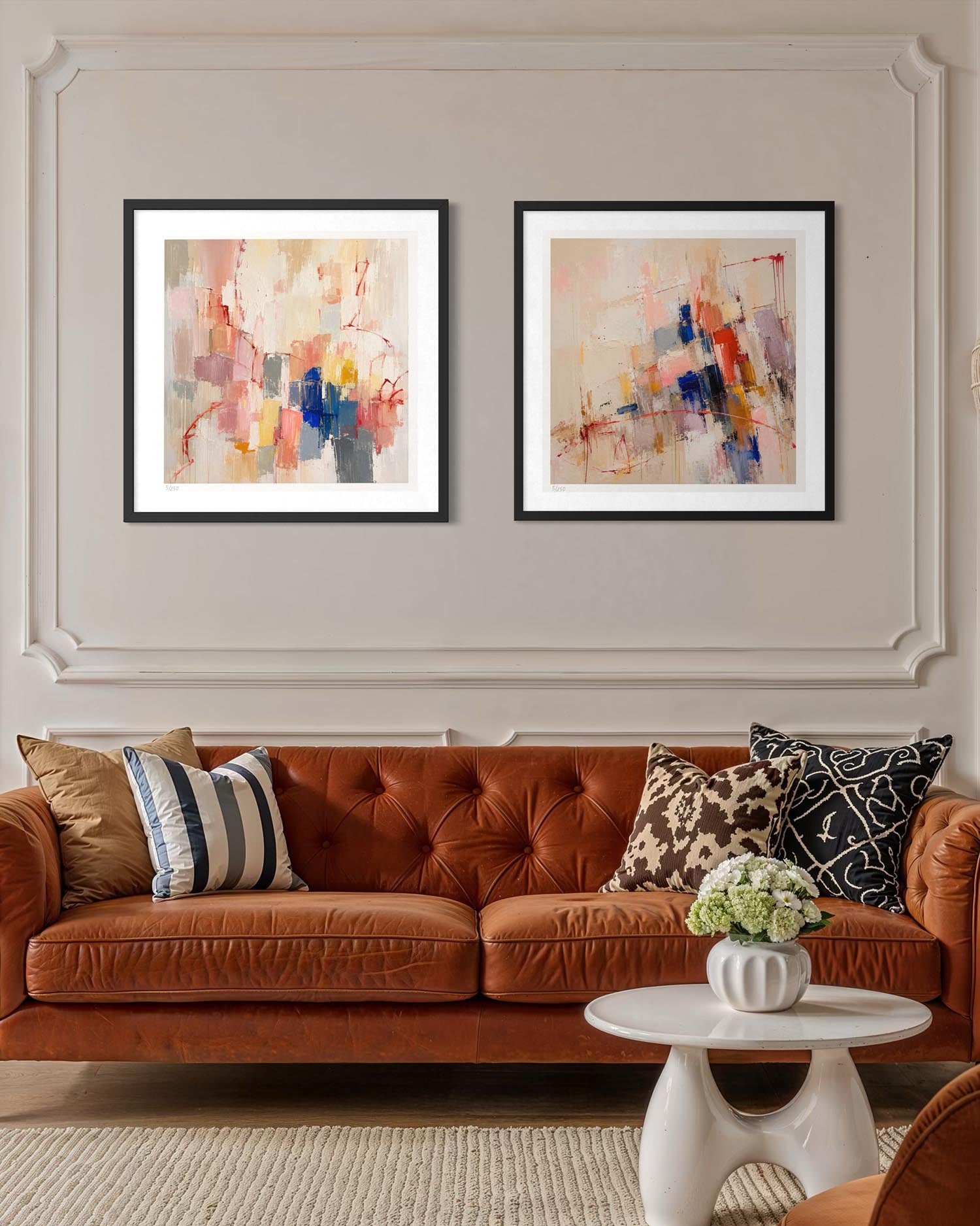 Two framed abstract art prints with black frames and white mats hang on a beige wall above a rust-brown tufted sofa with decorative throw pillows.