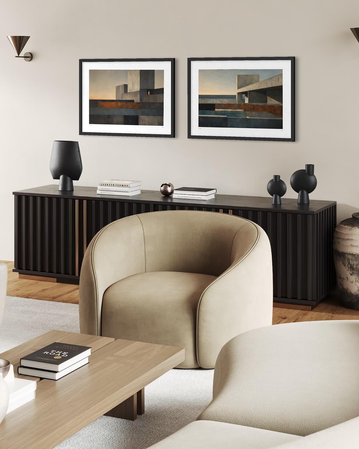 A styled living room interior featuring two framed abstract landscape prints with a black frame and white mat, displayed above a dark wood console. The room includes a beige upholstered armchair, a light wood coffee table, and neutral decor against a warm beige wall.