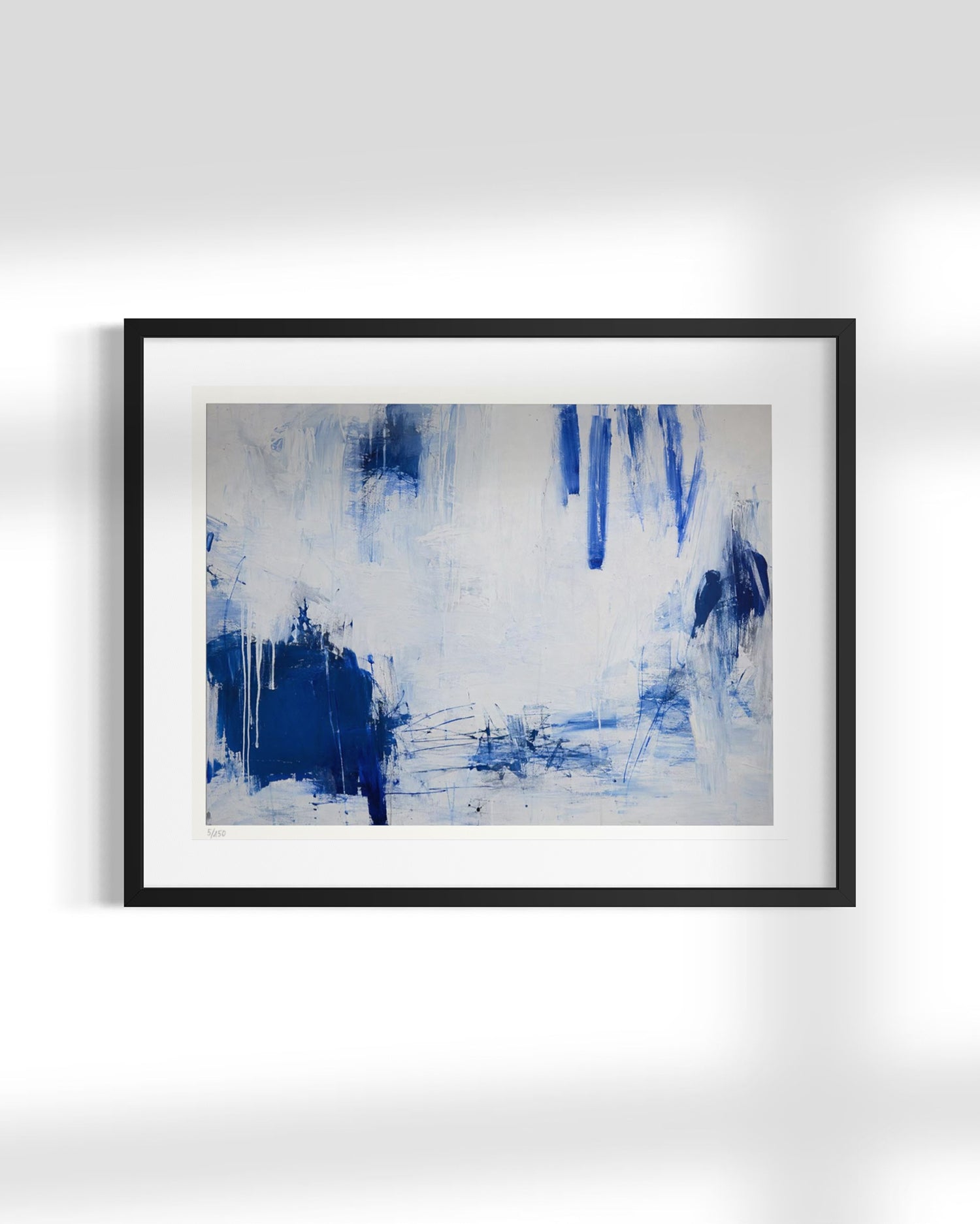 Framed abstract wall art featuring blue and white brushstrokes, presented in a black frame with a white mat against a light gray wall.