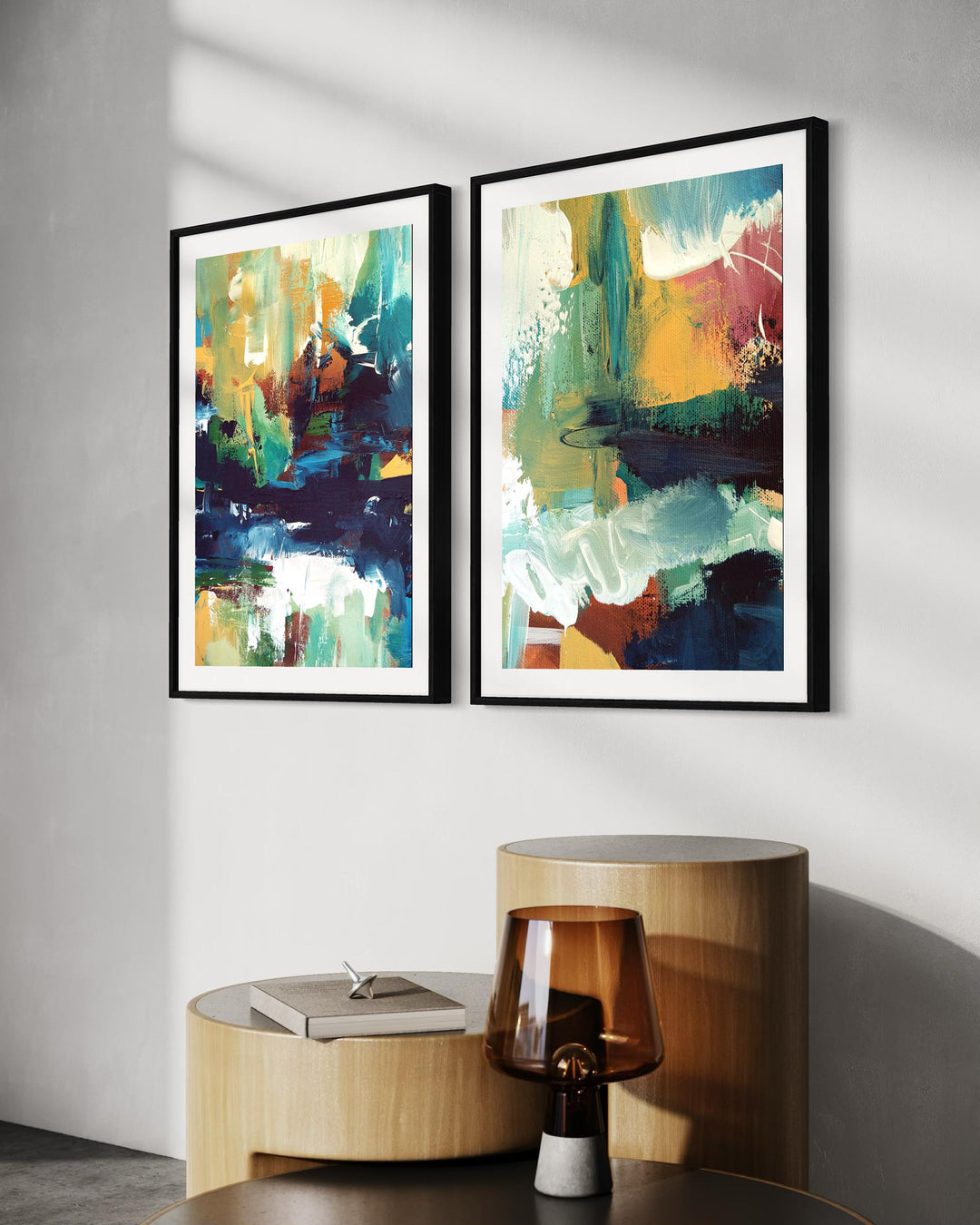 Two abstract art pieces on a wall above a round wooden table.
