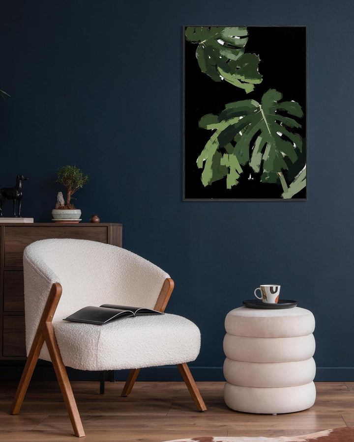 Modern living room with a white armchair, side table, and framed plant artwork on a dark blue wall.