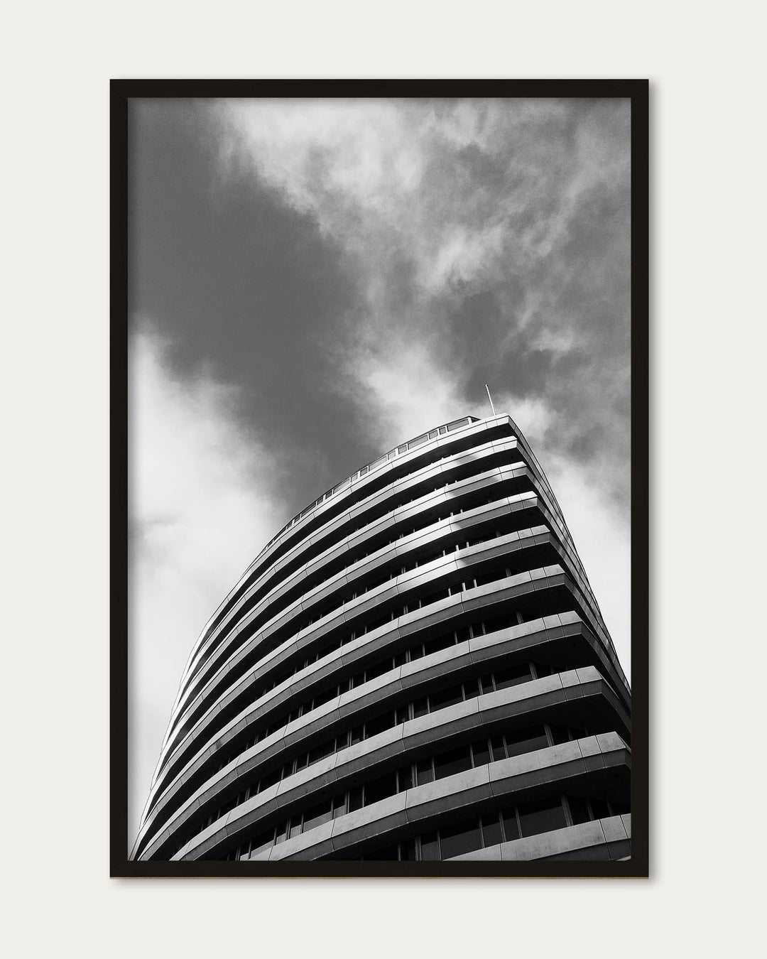 Framed black and white photograph of a curved building against a cloudy sky