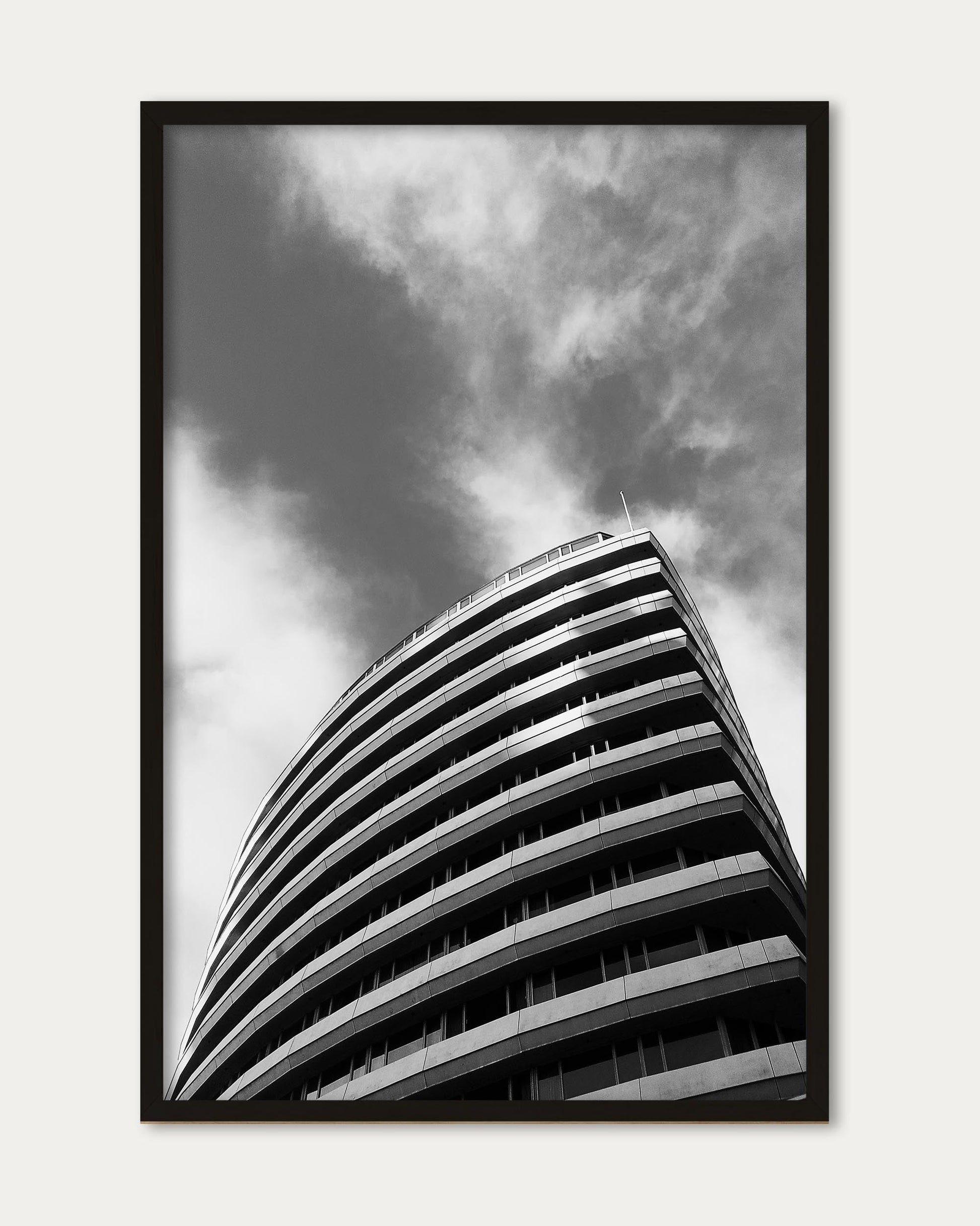 Framed black and white photograph of a curved building against a cloudy sky