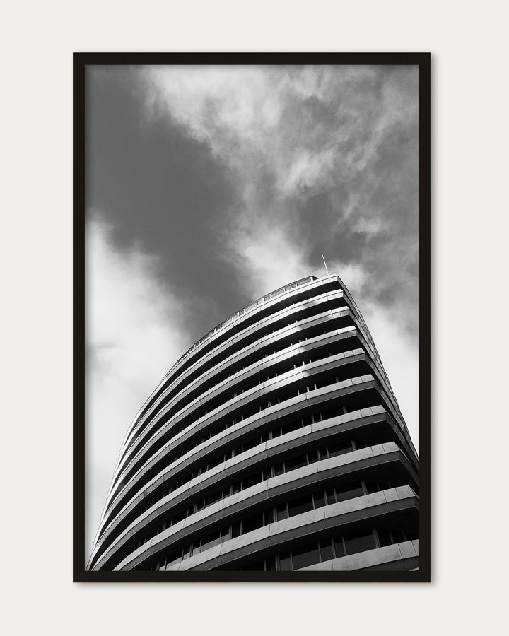 Framed black and white photograph of a curved building against a cloudy sky
