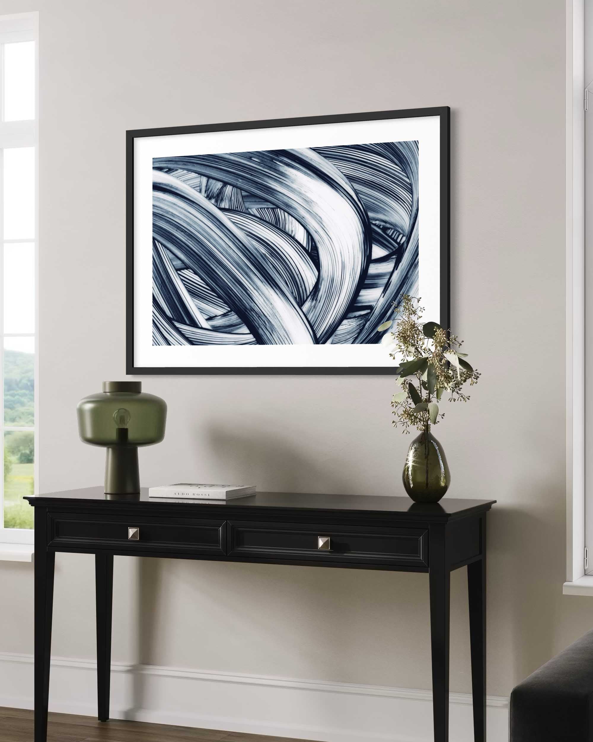 Framed abstract art on a wall above a black console table with decorative items.