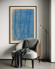 Gray armchair with a plaid pillow and gray blanket, framed blue abstract art on the wall, and a standing lamp.