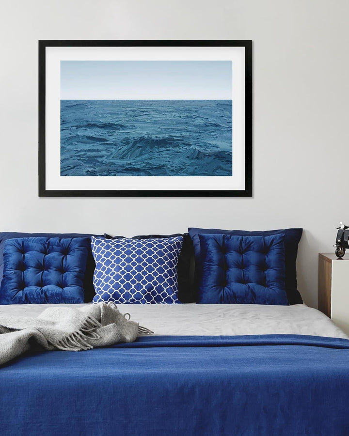 Framed artwork of a blue ocean scene above a bed with blue bedding and pillows.