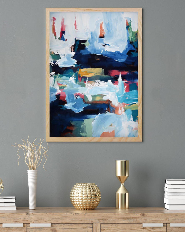 Abstract painting in a wooden frame on a gray wall above a wooden console table with decorative items.