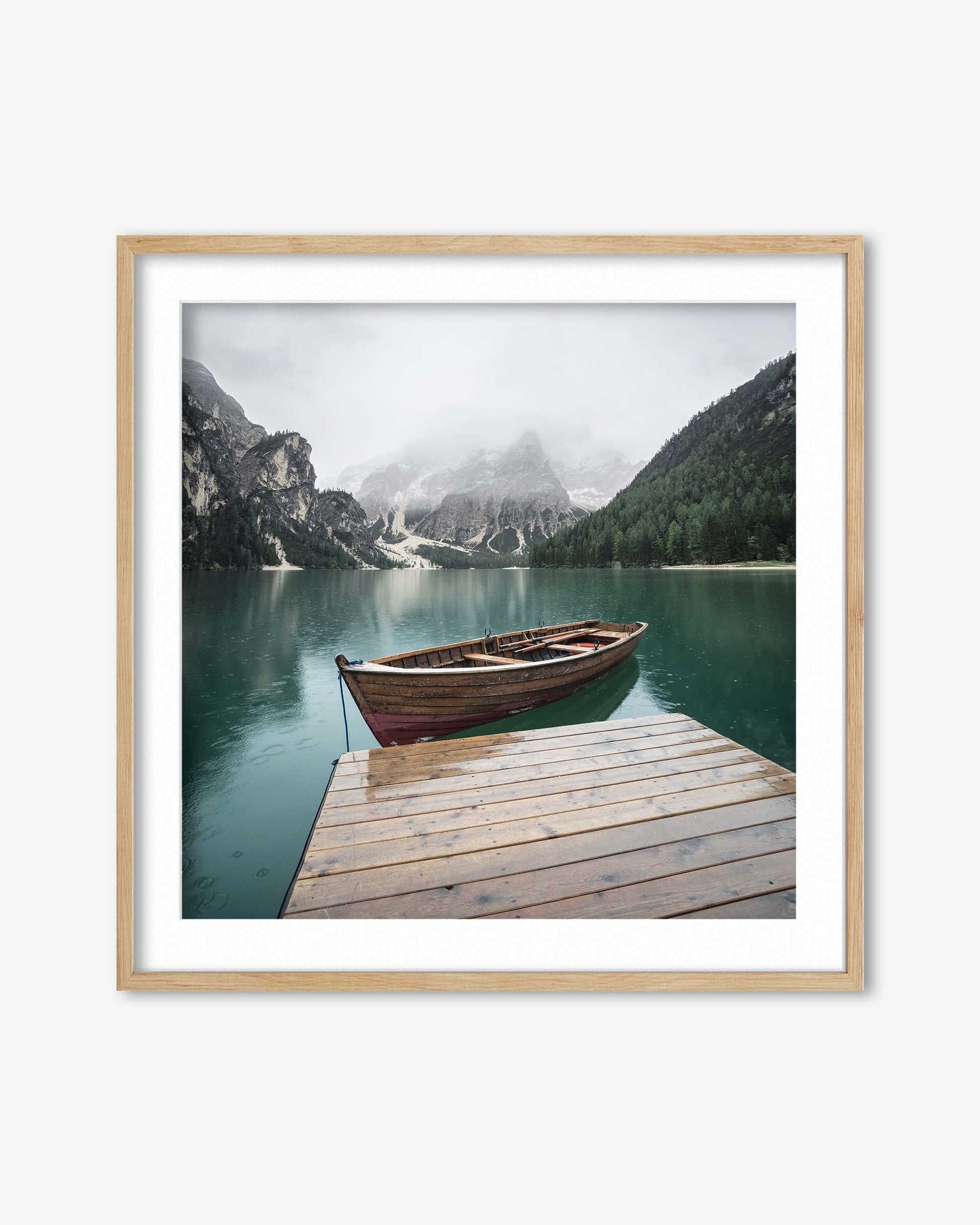 Framed photograph of a wooden boat on a dock with mountains and a lake in the background.
