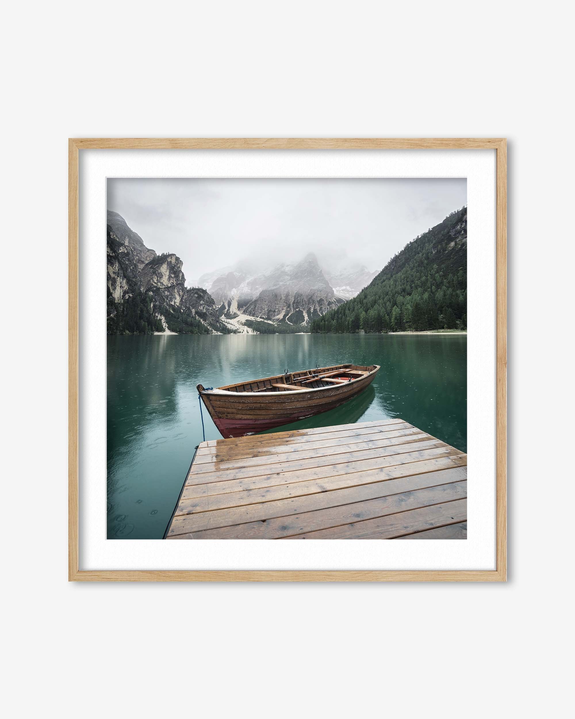 Framed photograph of a wooden boat on a dock with mountains and a lake in the background.