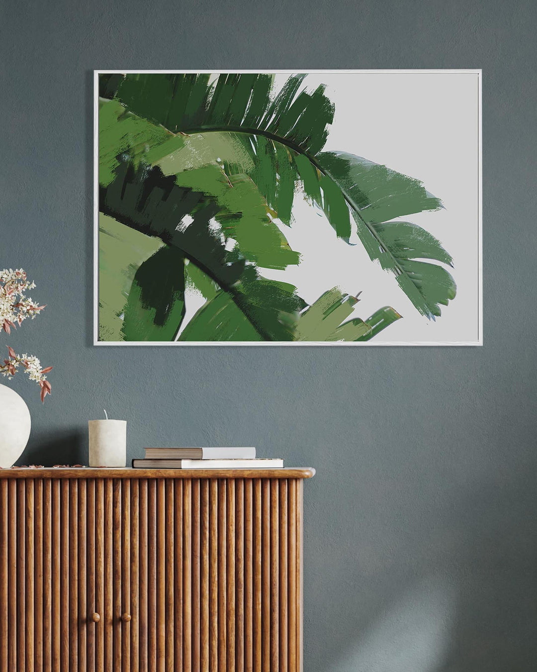 Framed artwork of green leaves above a wooden cabinet with decorative items.