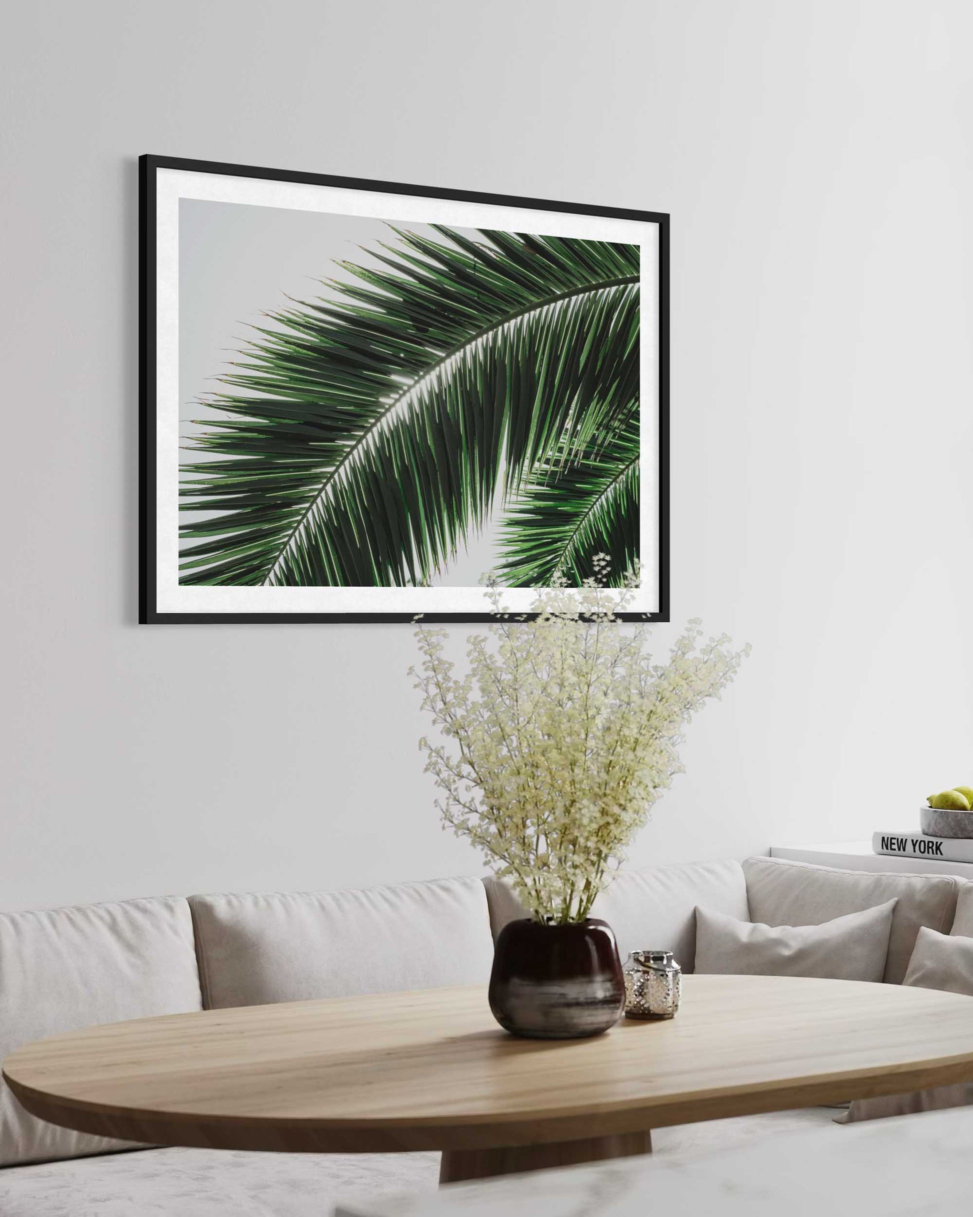 Framed artwork of a palm leaf on a wall above a living room table with decor items.