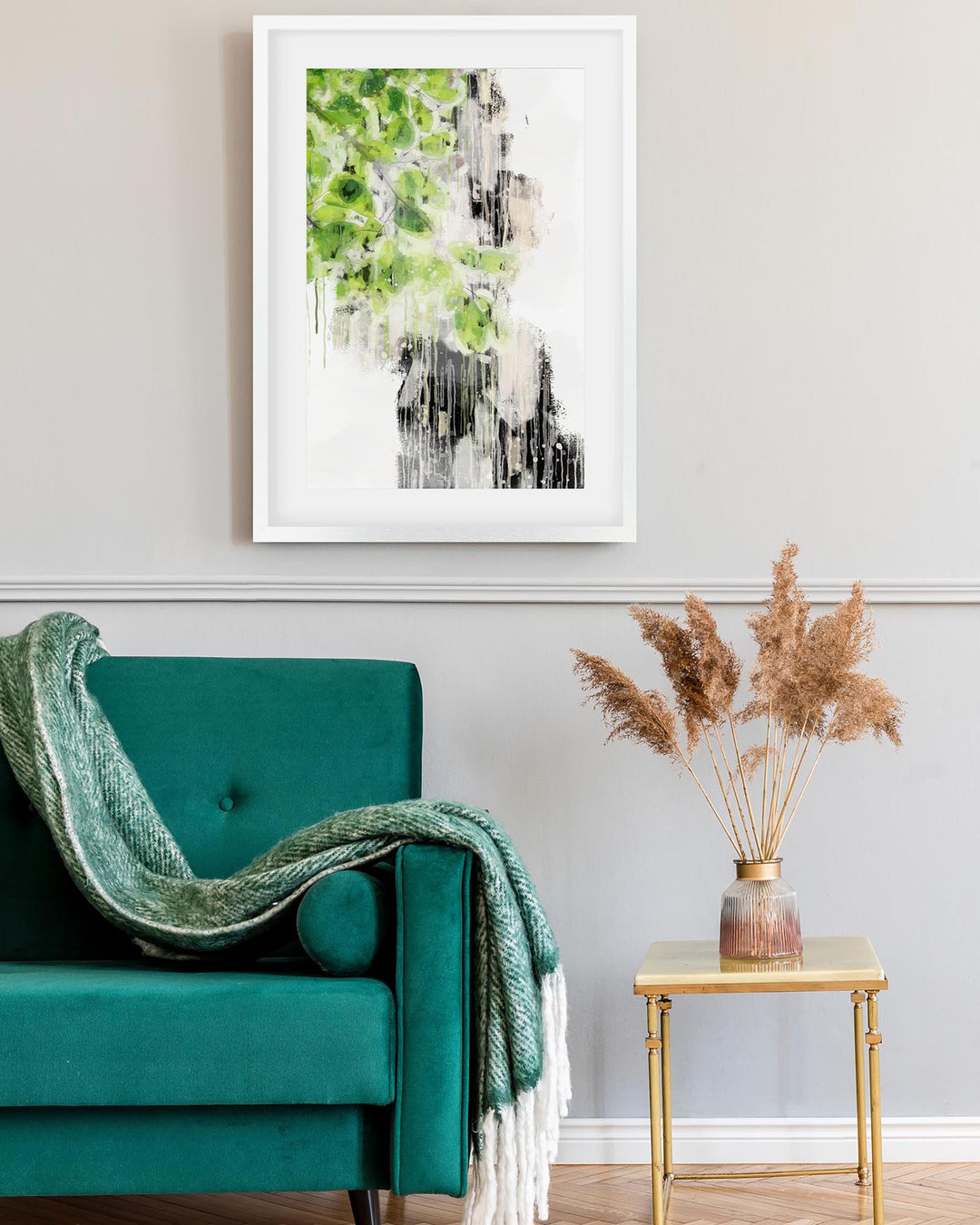 Teal armchair with a green blanket, framed abstract art on the wall, and a small table with dried plants.