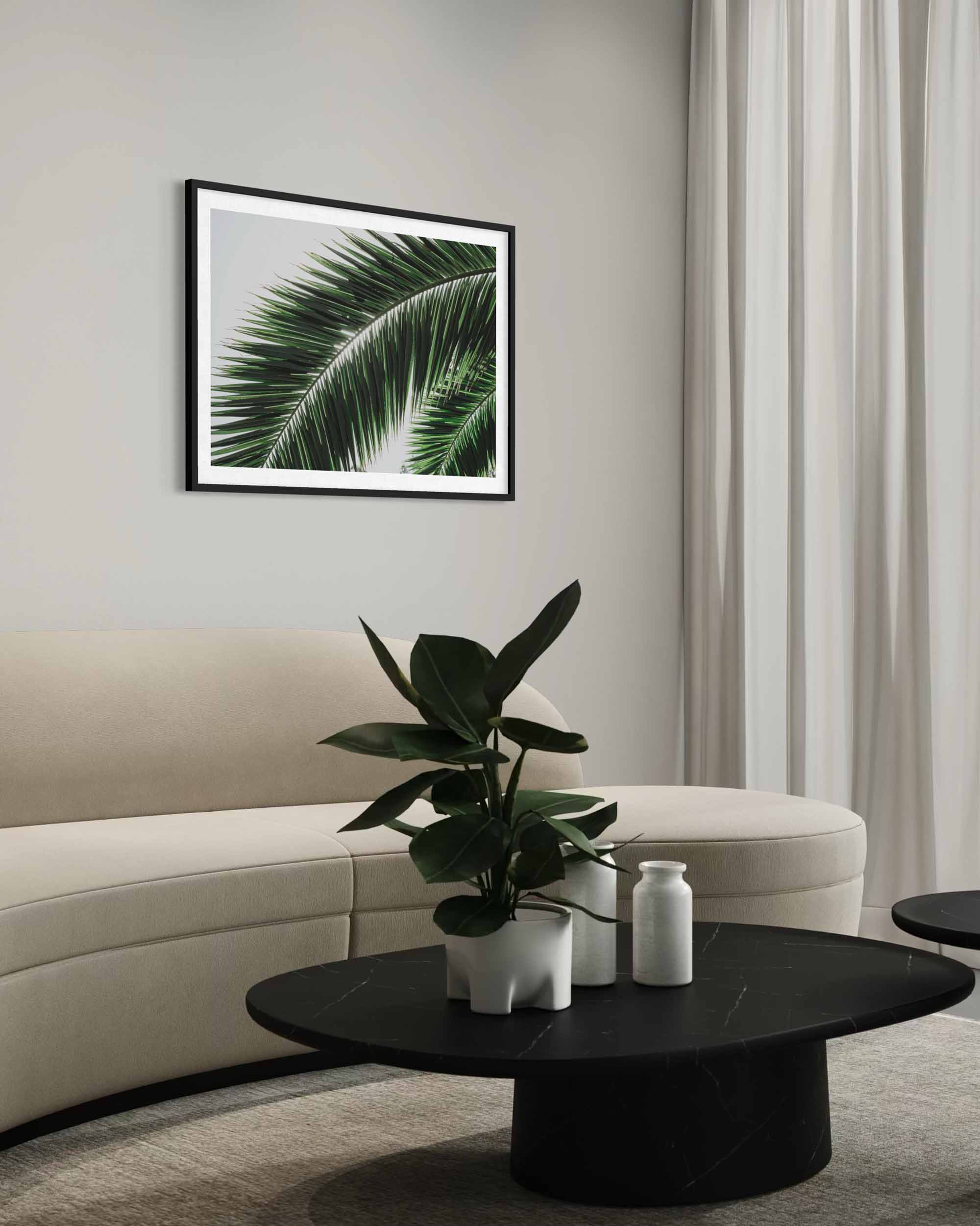 Modern living room with a framed palm leaf print on the wall, a beige sofa, and a black coffee table with a plant and vase.