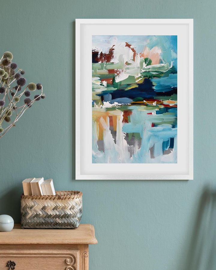 Framed abstract painting on a teal wall with a wooden cabinet and basket below.