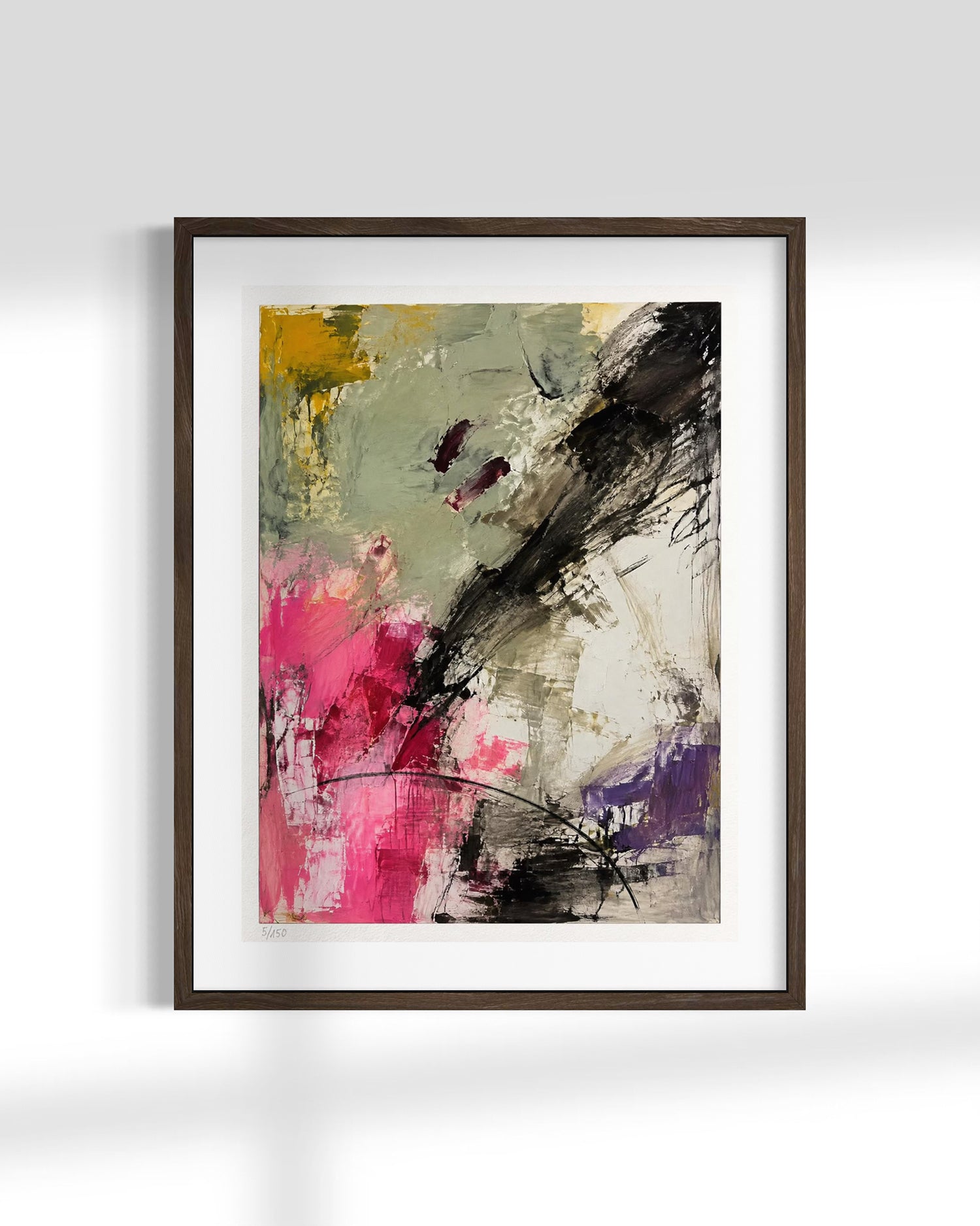A framed abstract art print featuring expressive brushstrokes in black, pink, purple, yellow, and gray on a white mat, set against a light gray wall.
