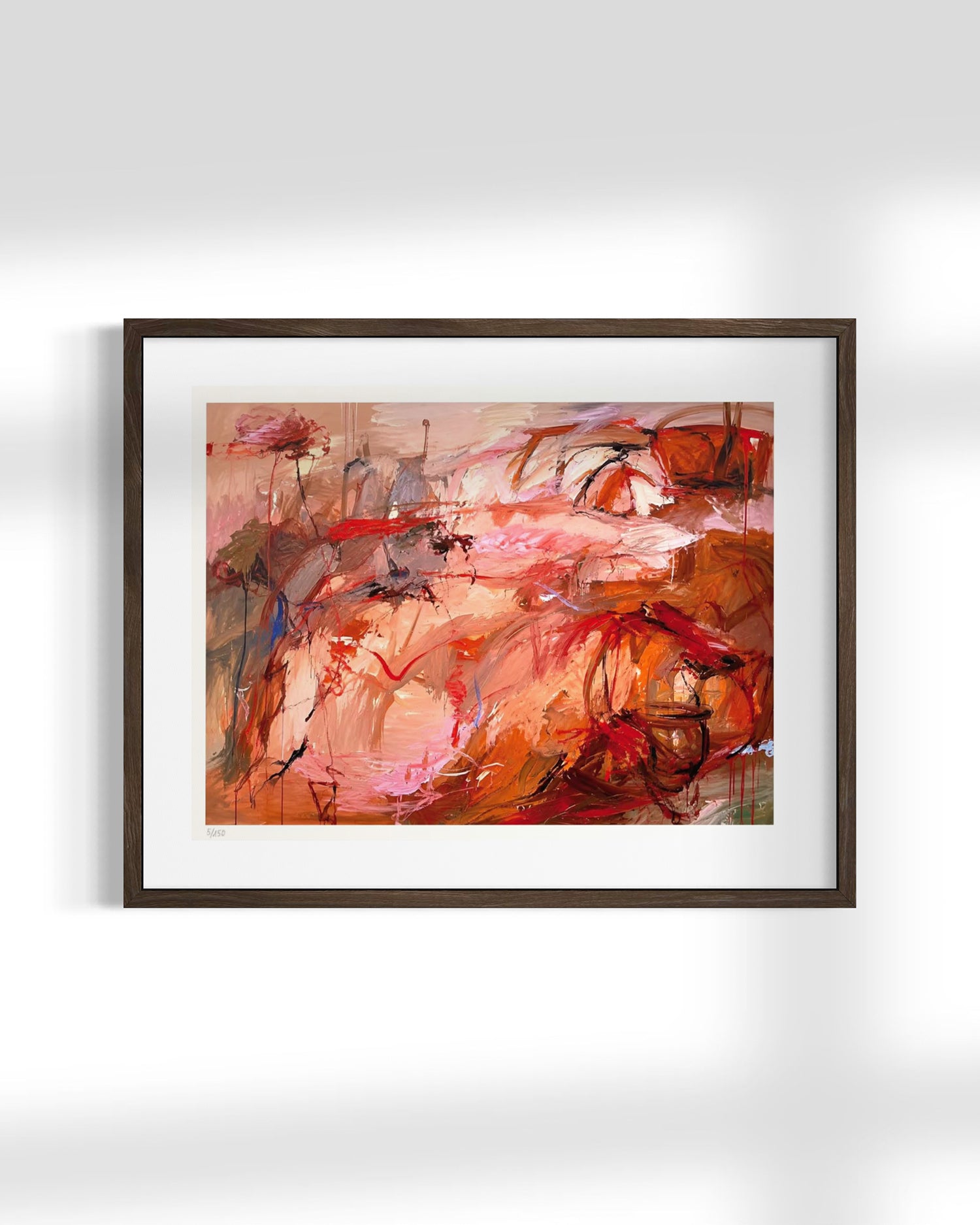 A framed abstract painting featuring expressive brushstrokes in warm tones of red, orange, pink, and brown, presented in a dark wood frame with a white mat against a light gray wall.