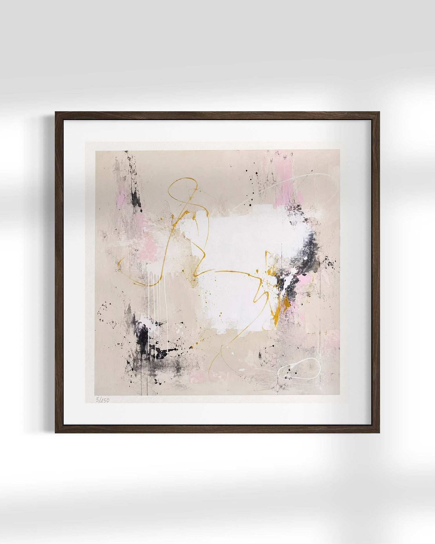 Framed abstract wall art hanging on a light gray wall, featuring a white center with pink, black, and gold brushstrokes and splatters, set in a dark brown frame with a white mat.