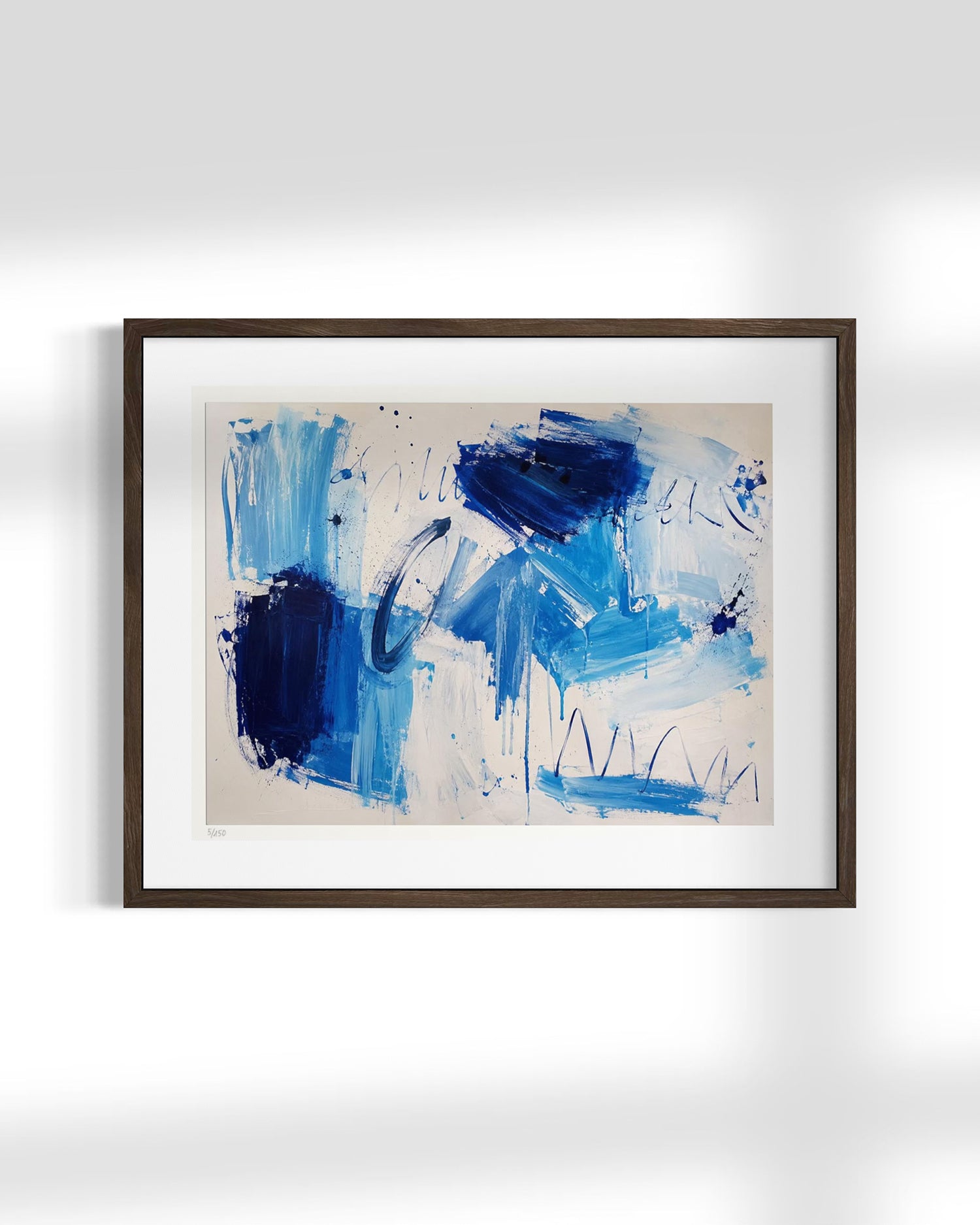 A framed abstract art print featuring blue and navy brushstrokes on a cream background, enclosed in a dark brown frame and displayed against a light gray wall.