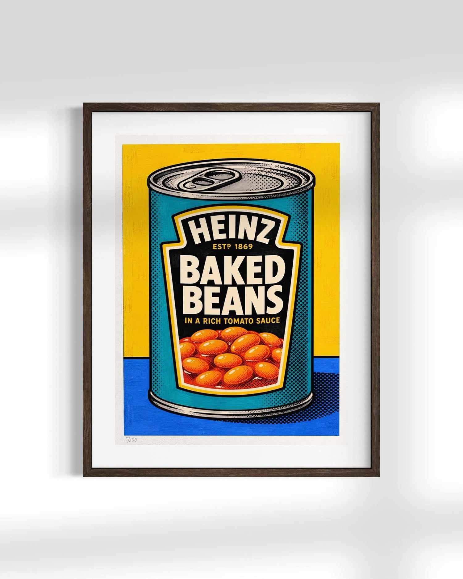 A framed pop-art print of a vintage Heinz Baked Beans can, featuring a yellow and blue background with the beans visible at the bottom of the can, shown against a light gray wall.
