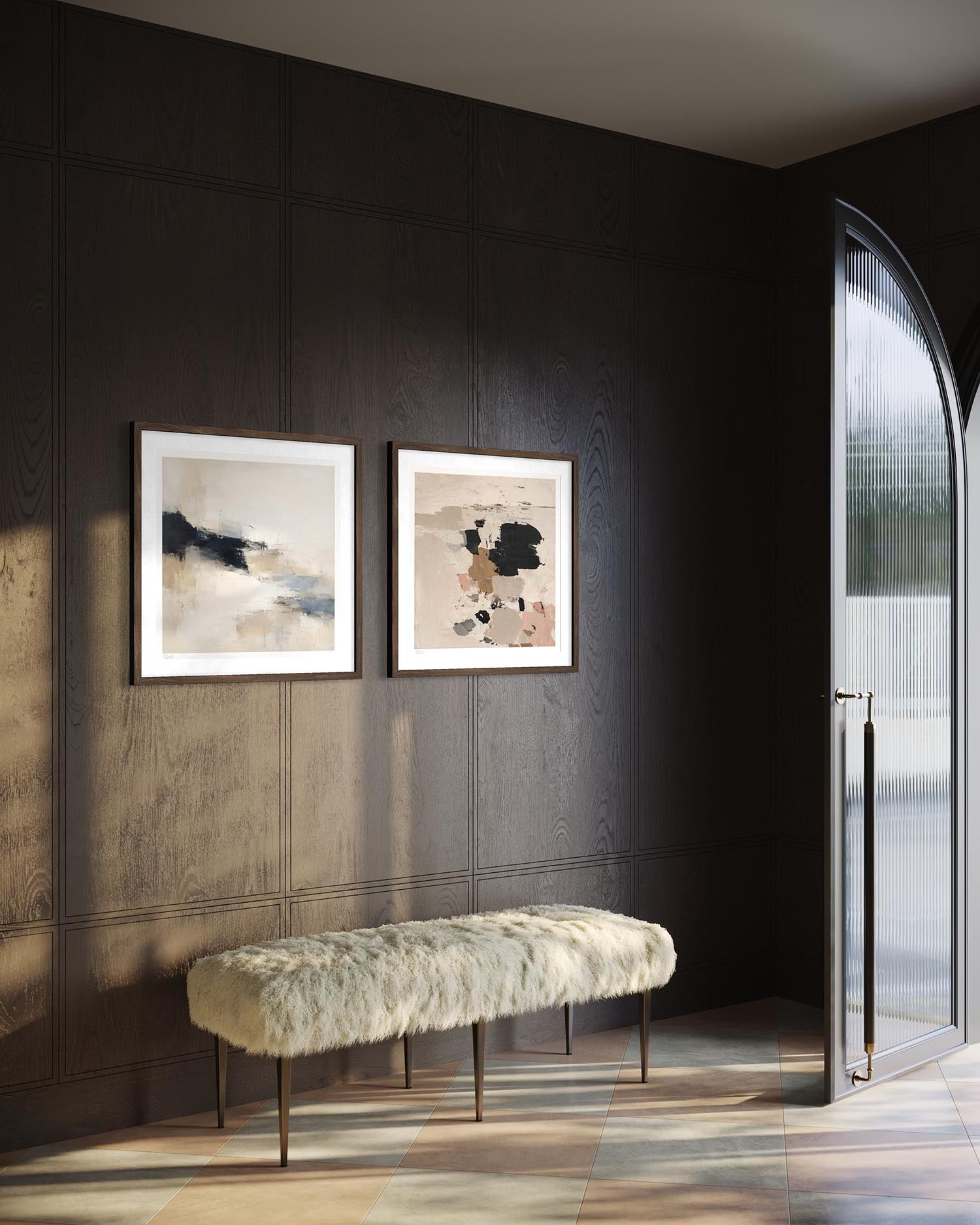 Two framed abstract art prints hang on a dark wood-paneled wall above a white faux-fur bench in a modern interior setting with a glass door.