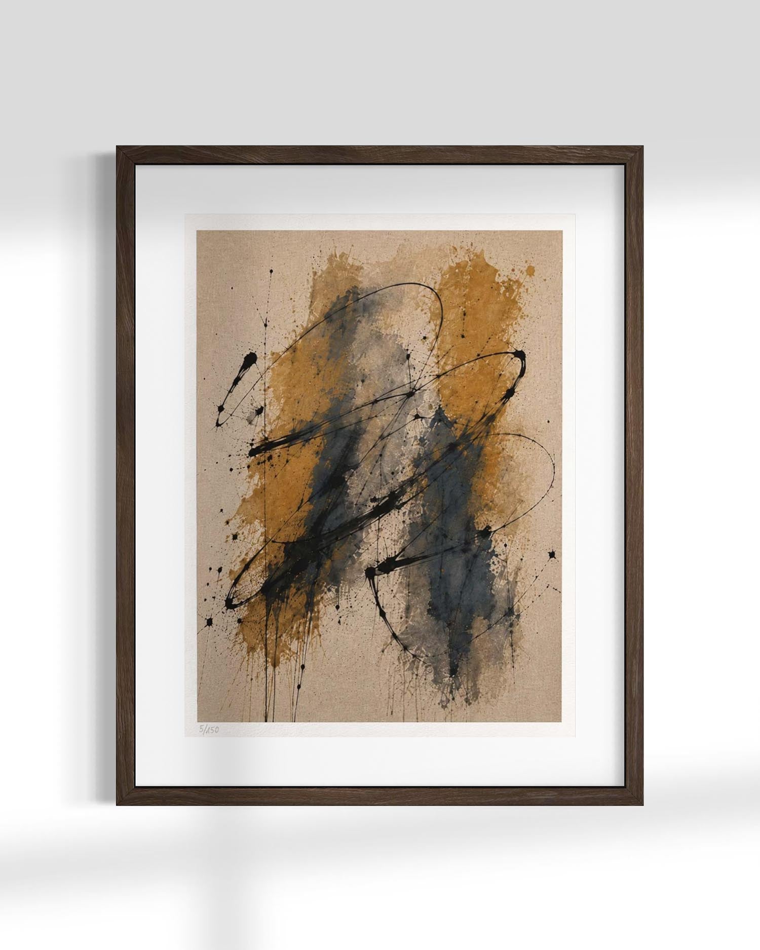 Framed abstract wall art featuring expressive black and ochre-orange paint splatters and drips on a warm beige background, presented in a dark wood frame with a white mat against a light gray wall.