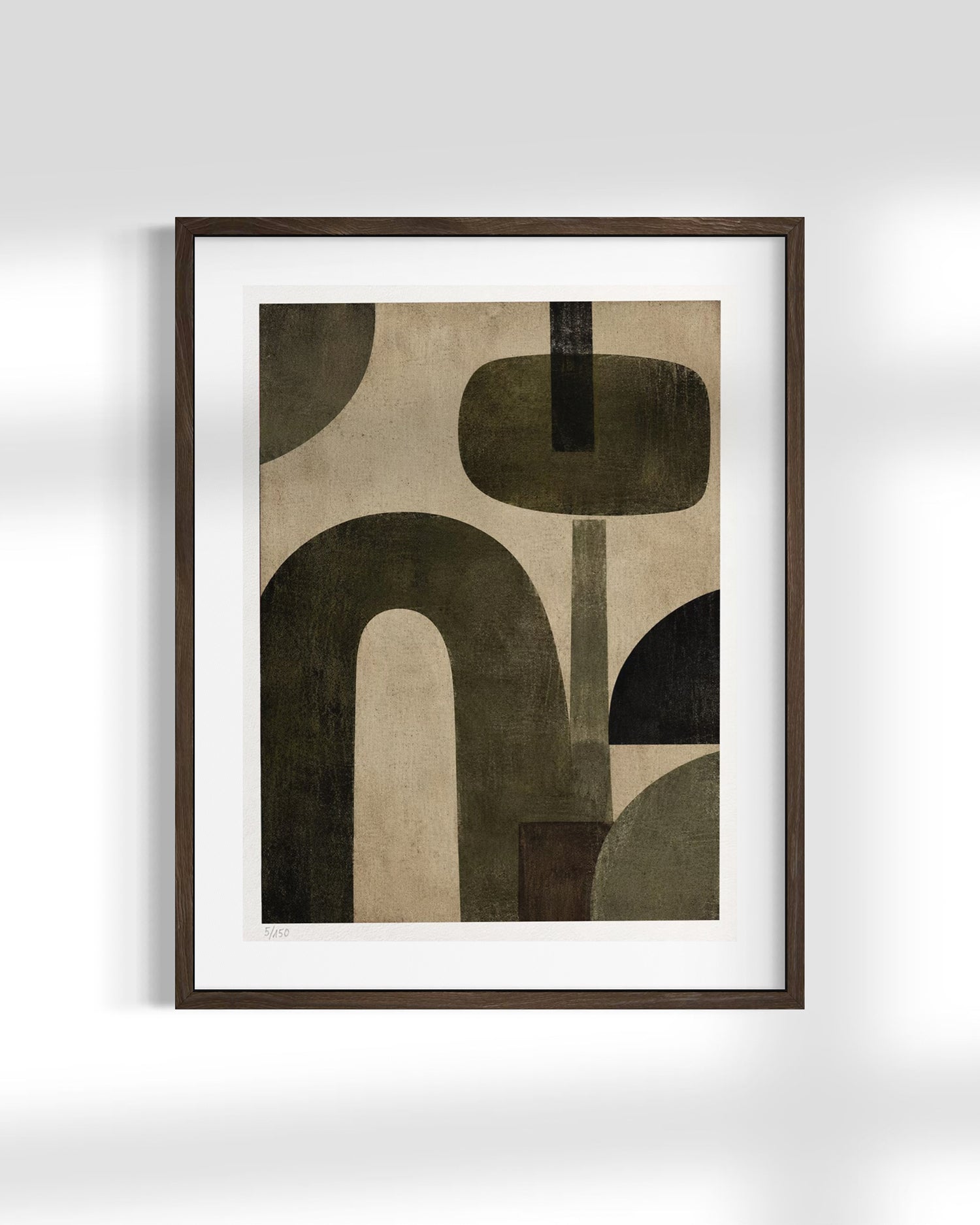 Framed abstract wall art featuring organic geometric shapes in dark olive green, charcoal, and beige on a white mat, set in a dark brown frame against a light gray wall.