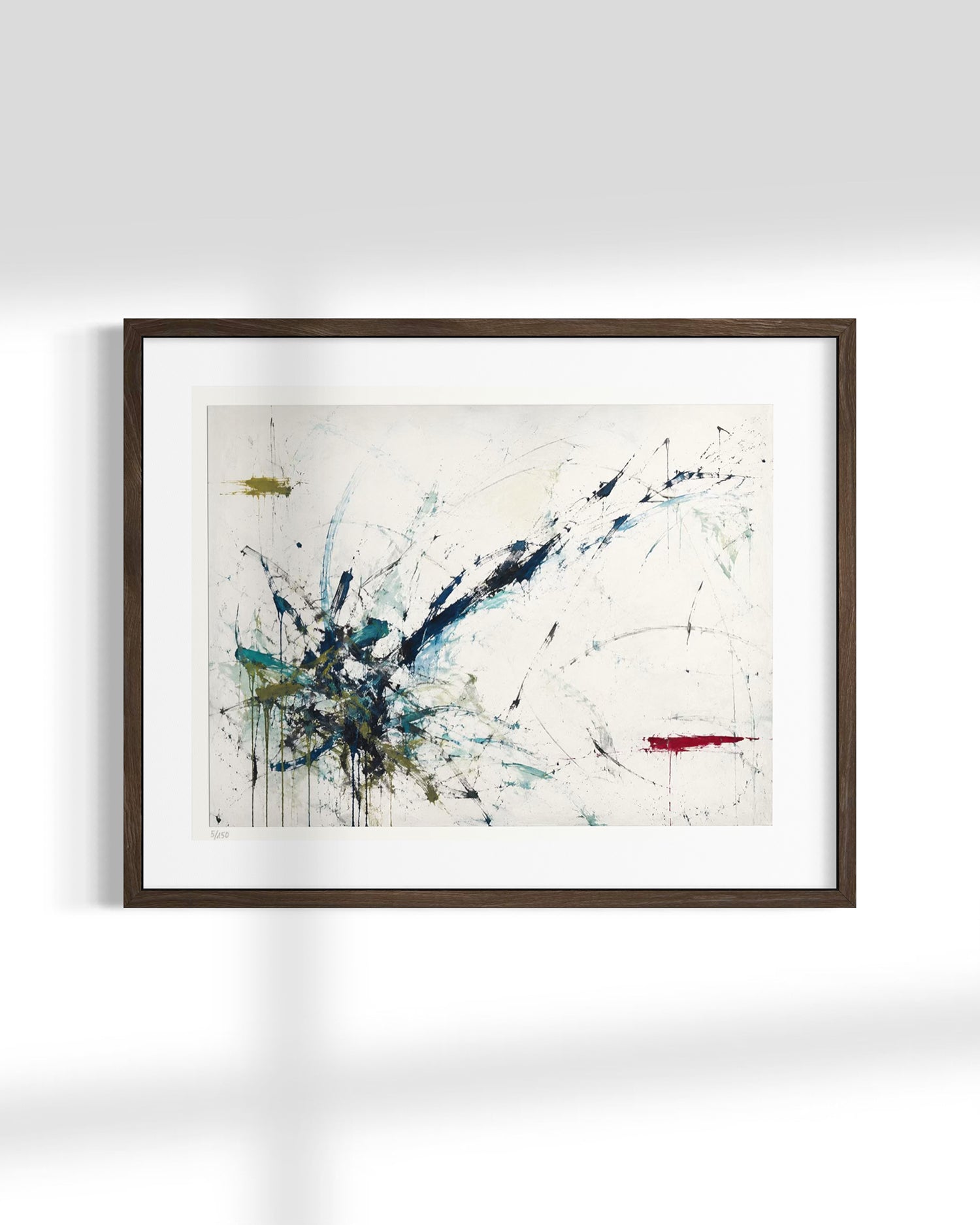 Framed abstract wall art hanging on a white wall, featuring expressive blue, black, teal, and red paint splatters on an off-white background, enclosed in a dark wood frame with a white mat.