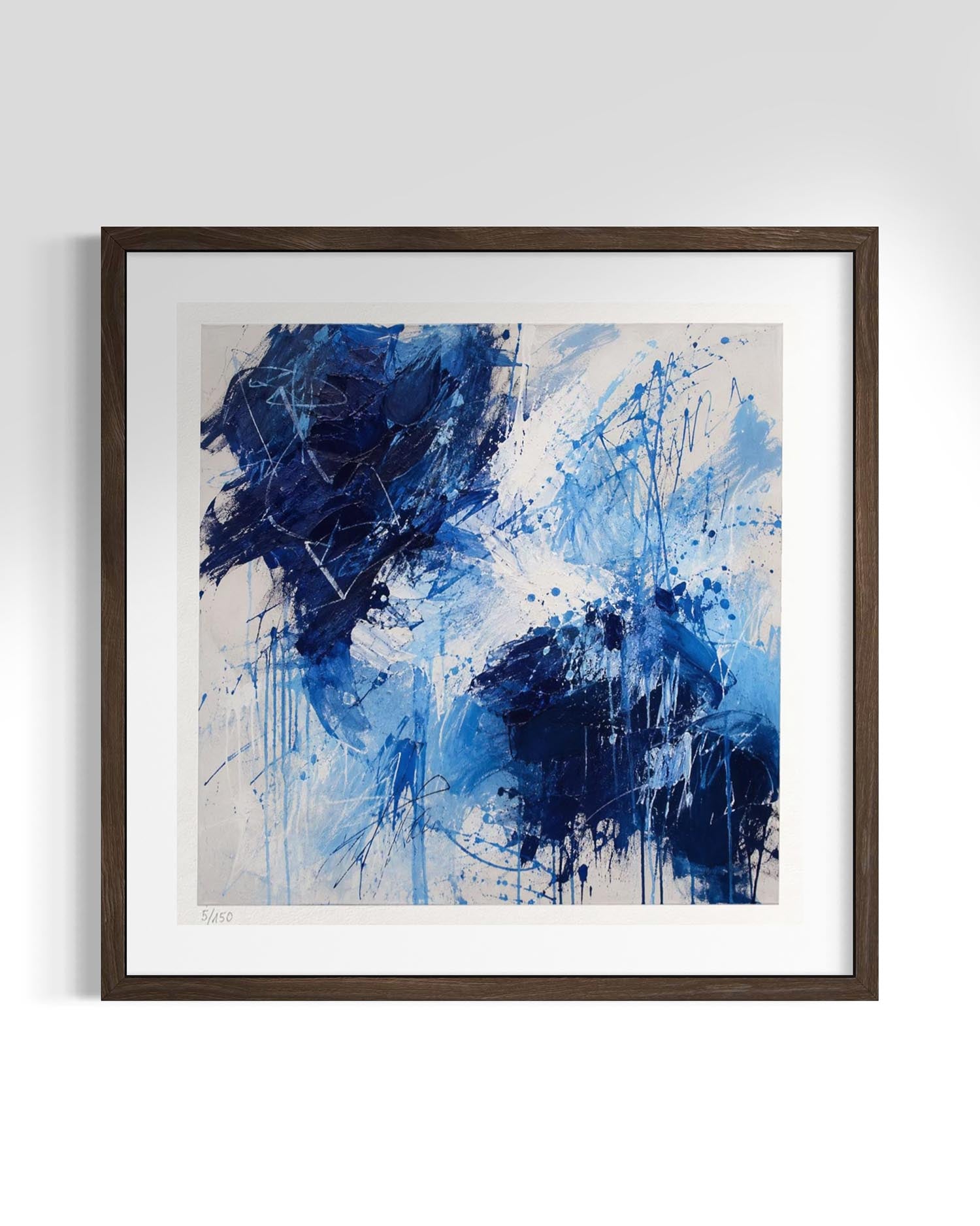Framed abstract wall art featuring expressive blue and navy brushstrokes and splatters on a light beige background, presented in a dark brown wooden frame with a white mat against a clean white wall.