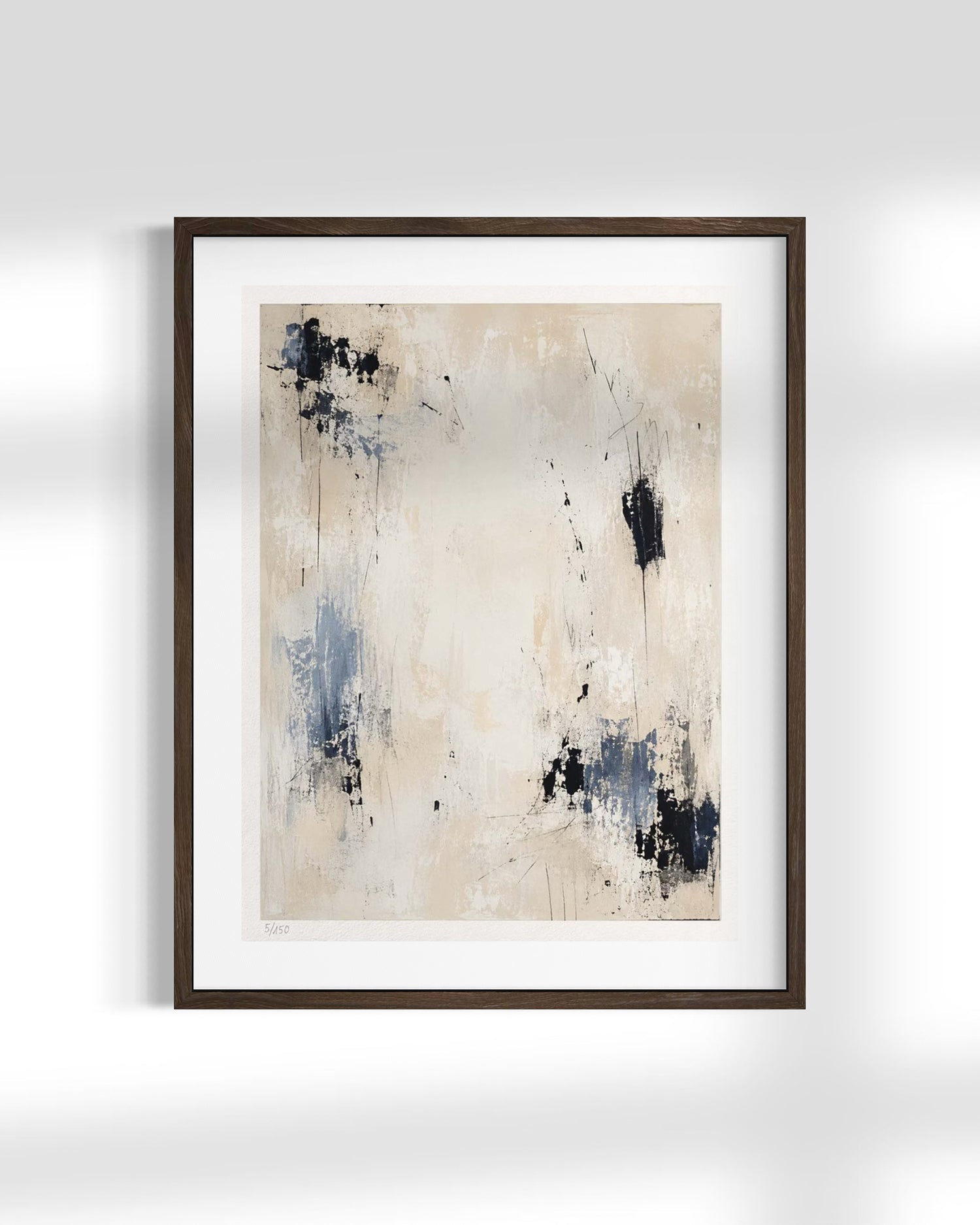 Framed abstract wall art featuring a minimalist beige and cream background with blue and black paint splatters, presented in a dark brown frame against a light gray wall.