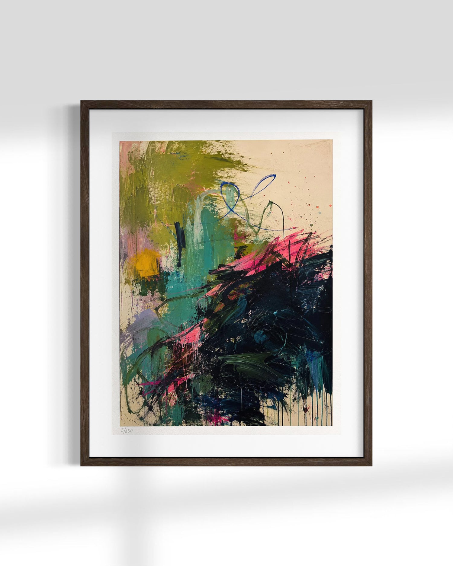 A framed abstract art print featuring expressive brushstrokes in green, teal, black, pink, and yellow on a beige background, enclosed in a dark brown frame with a white mat, displayed against a light gray wall.