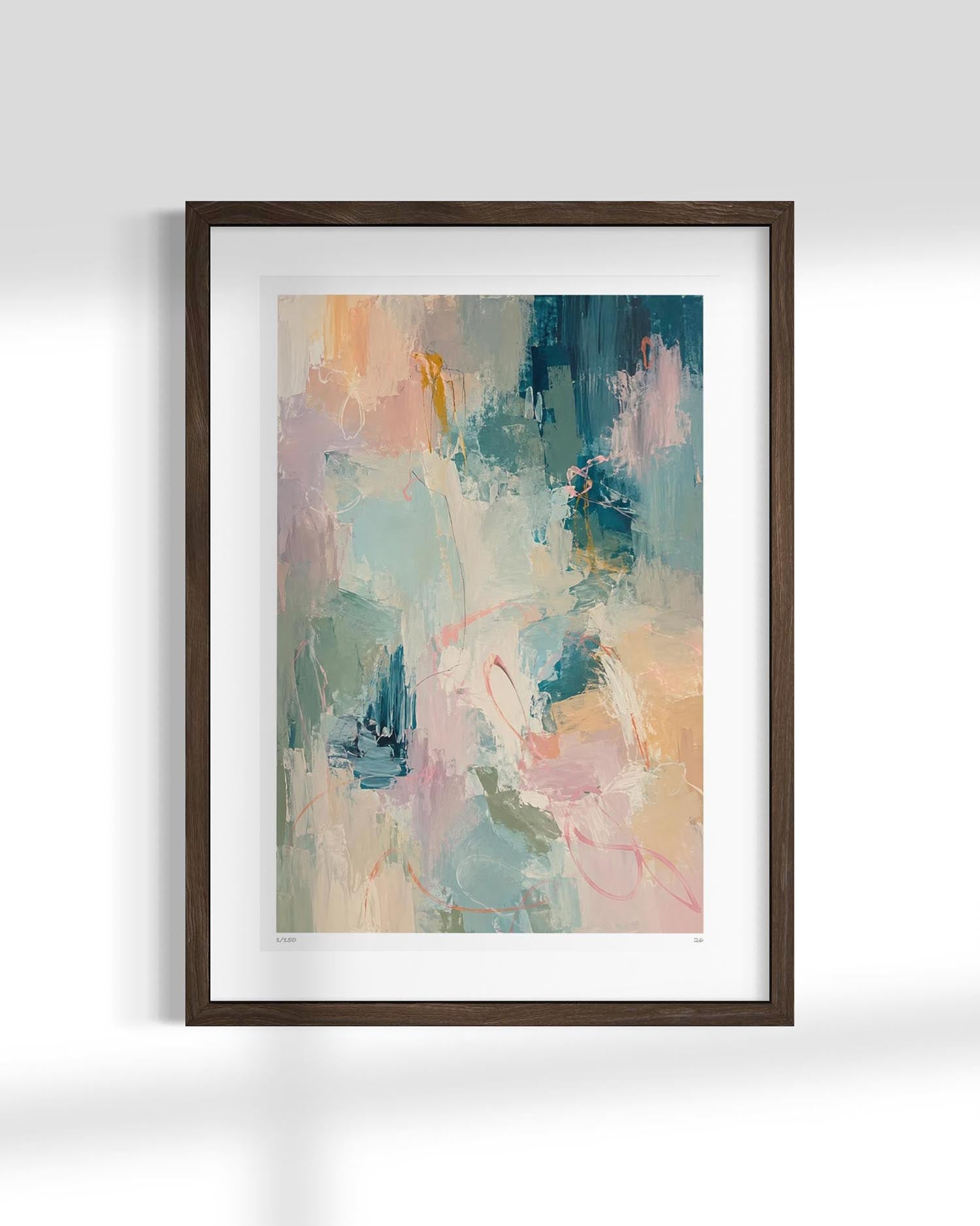A framed abstract art print featuring a colorful painting with soft brushstrokes in teal, pink, peach, and cream, set in a dark brown wooden frame with a white mat against a light gray wall.