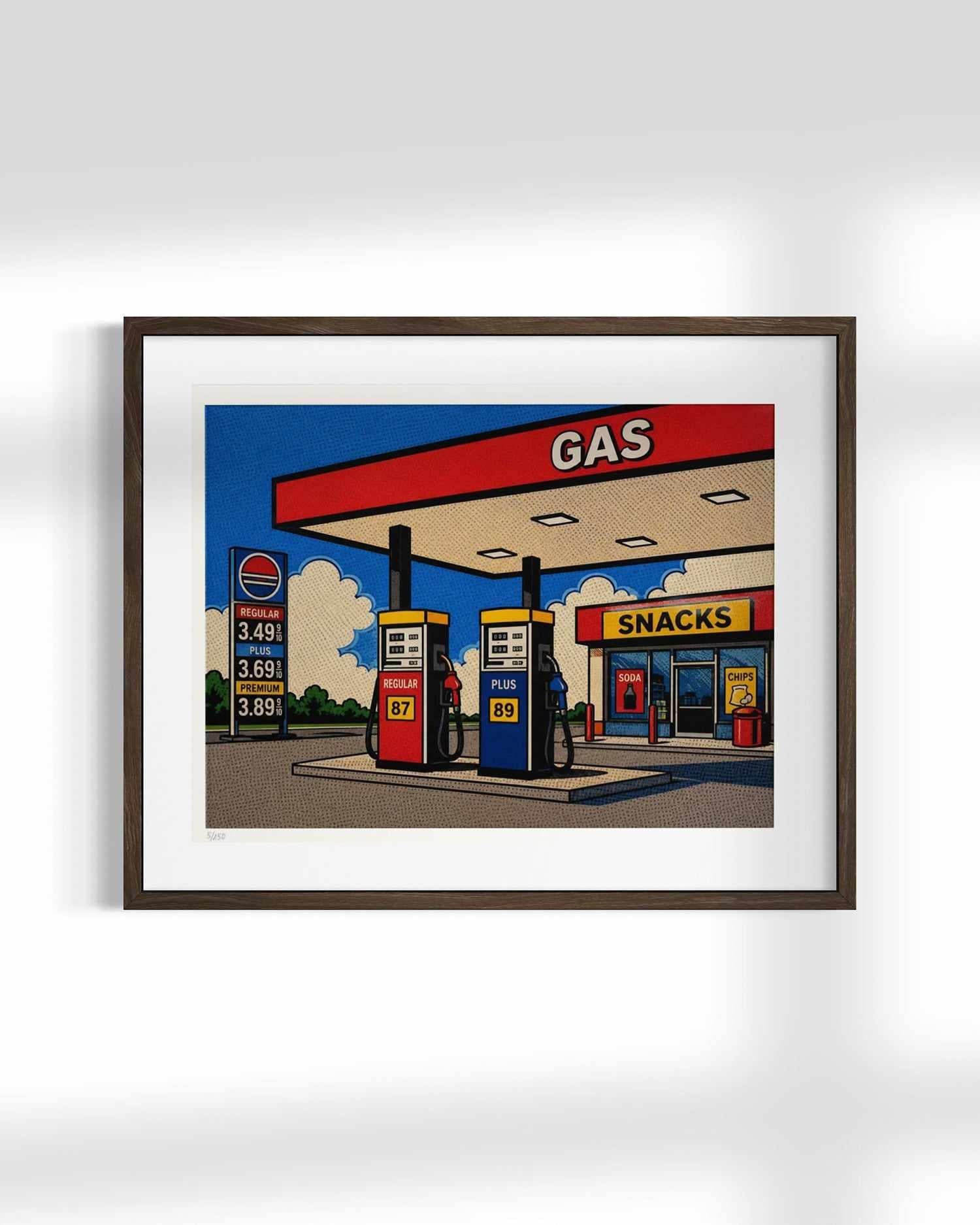 A framed pop-art style illustration of a gas station and convenience store, shown hanging on a light gray wall. The artwork features bold comic-like colors with a red gas canopy, blue sky, fuel pumps, and a snack shop under a sign reading 'SNACKS'.
