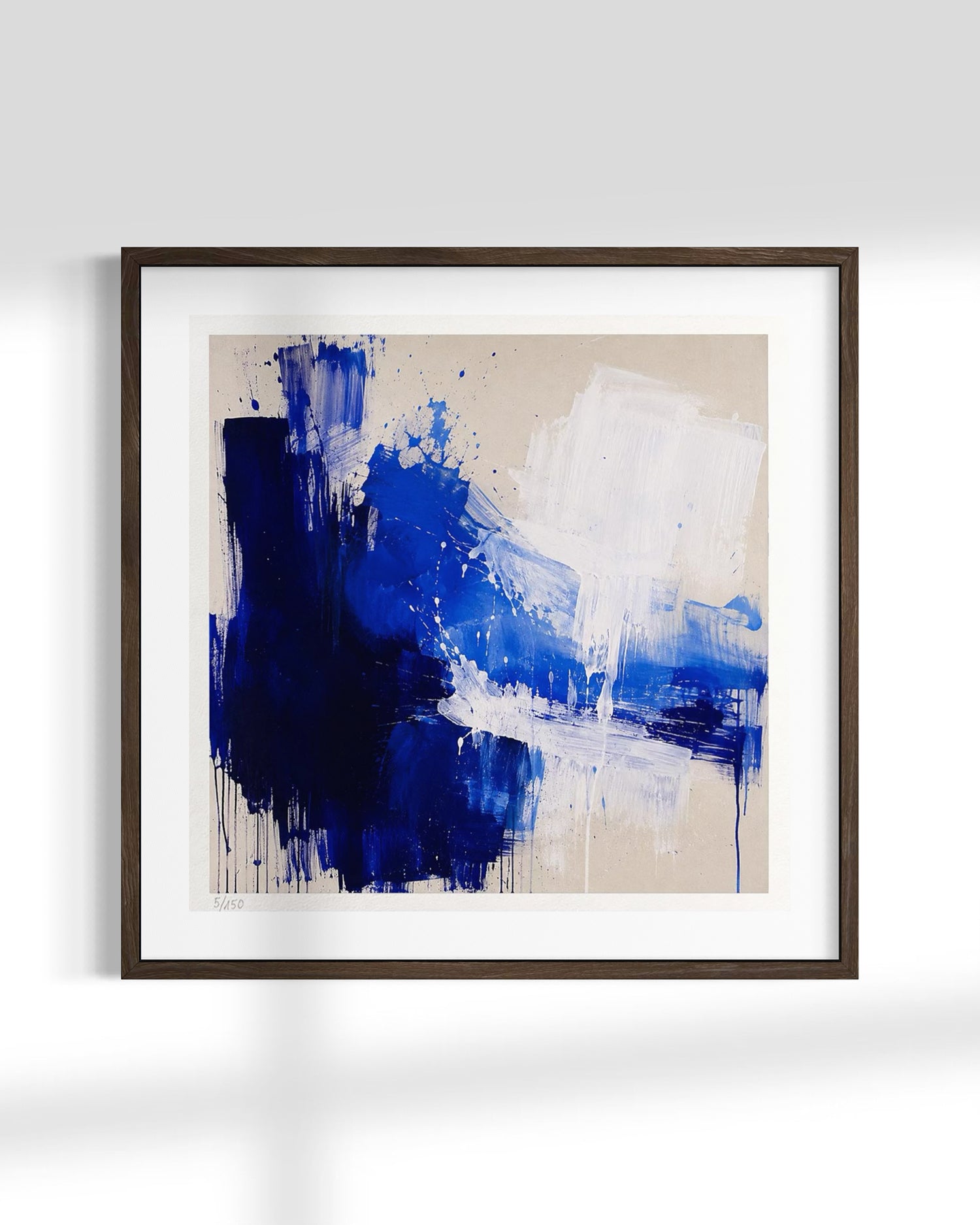 Framed abstract wall art featuring bold blue and white paint strokes on a warm beige background, presented in a dark wood frame with a white mat against a light gray wall.