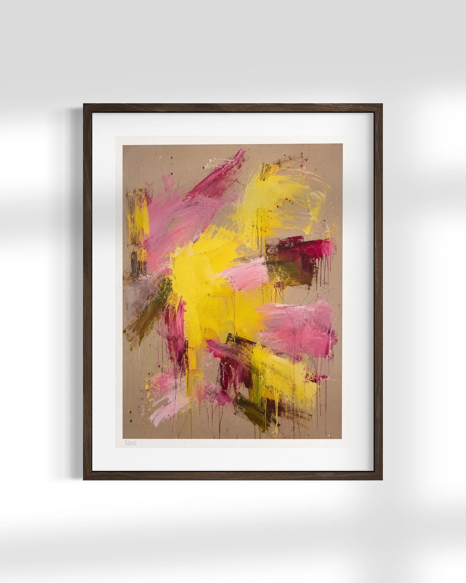 Framed abstract wall art featuring expressive brushstrokes in yellow, pink, and brown on a beige background, presented in a dark wood frame with a white mat against a light gray wall.