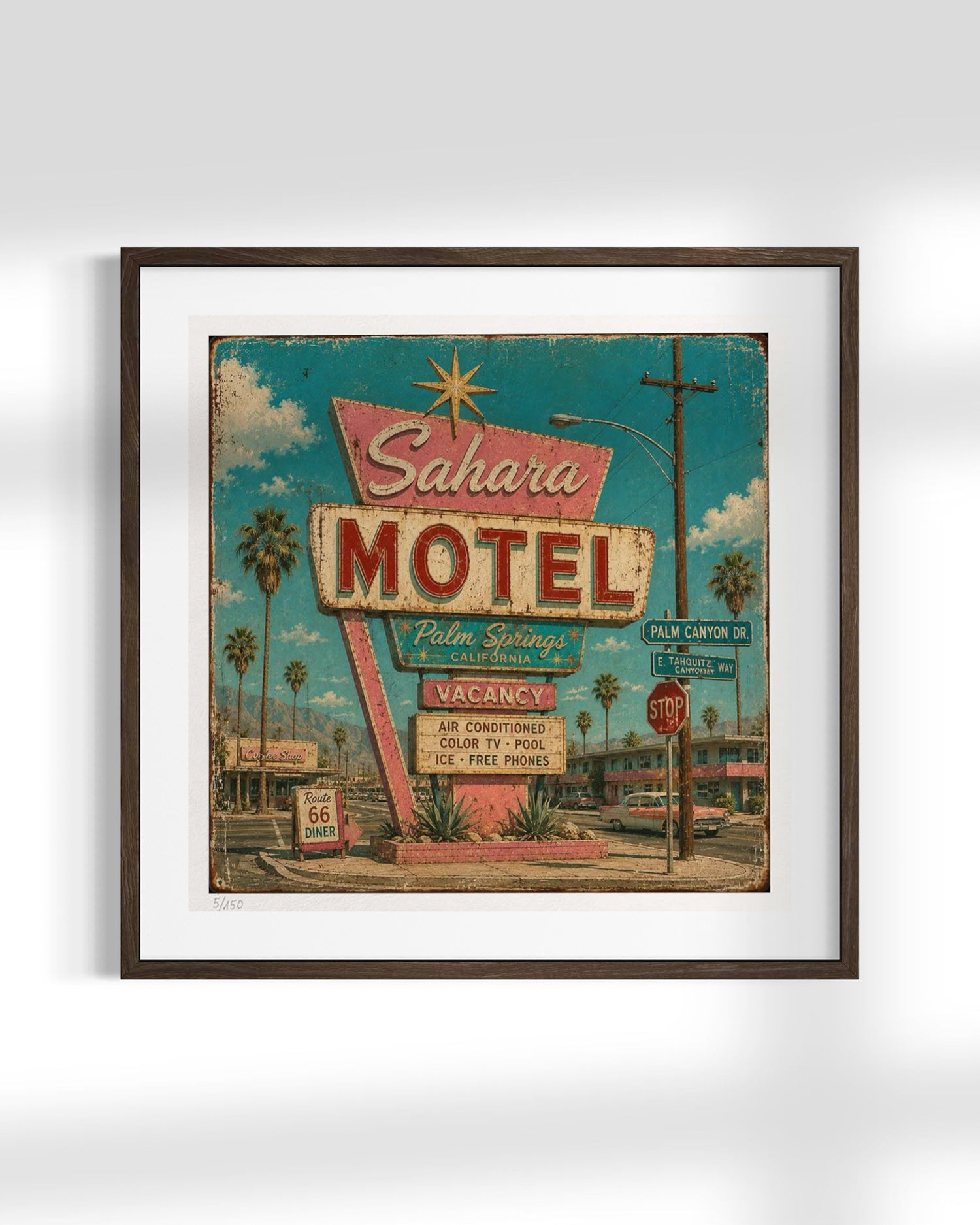 Framed wall art featuring a retro-style illustration of the Sahara Motel sign, with palm trees, a street scene, and a turquoise sky, shown in a dark wood frame against a light gray background.