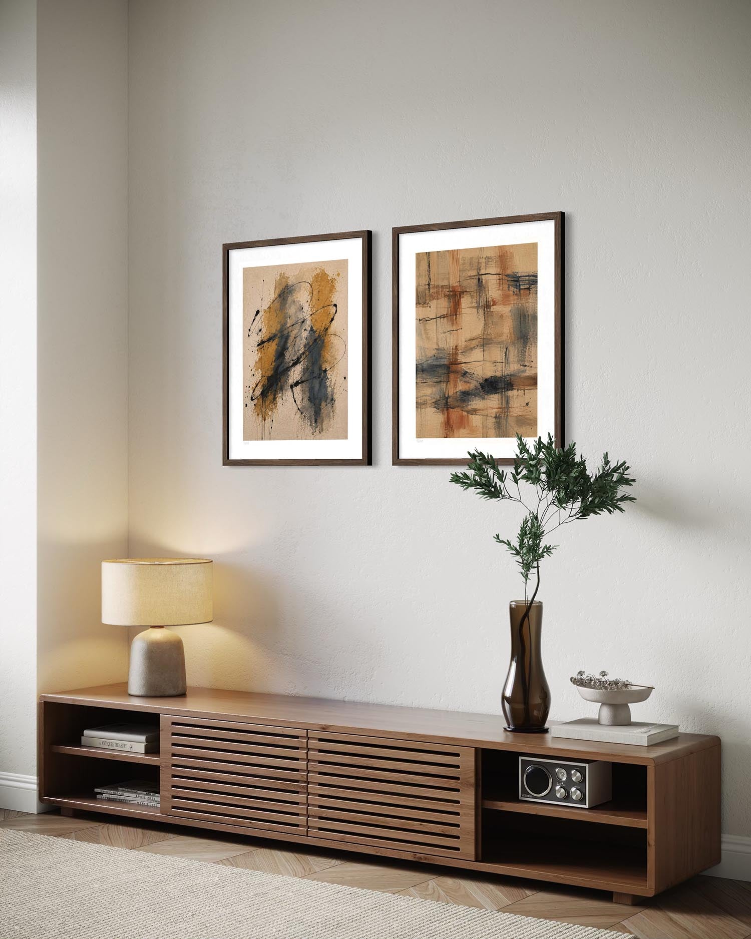 Two framed abstract art prints with white mats hang on a light gray wall above a wooden media console in a styled living room setting.