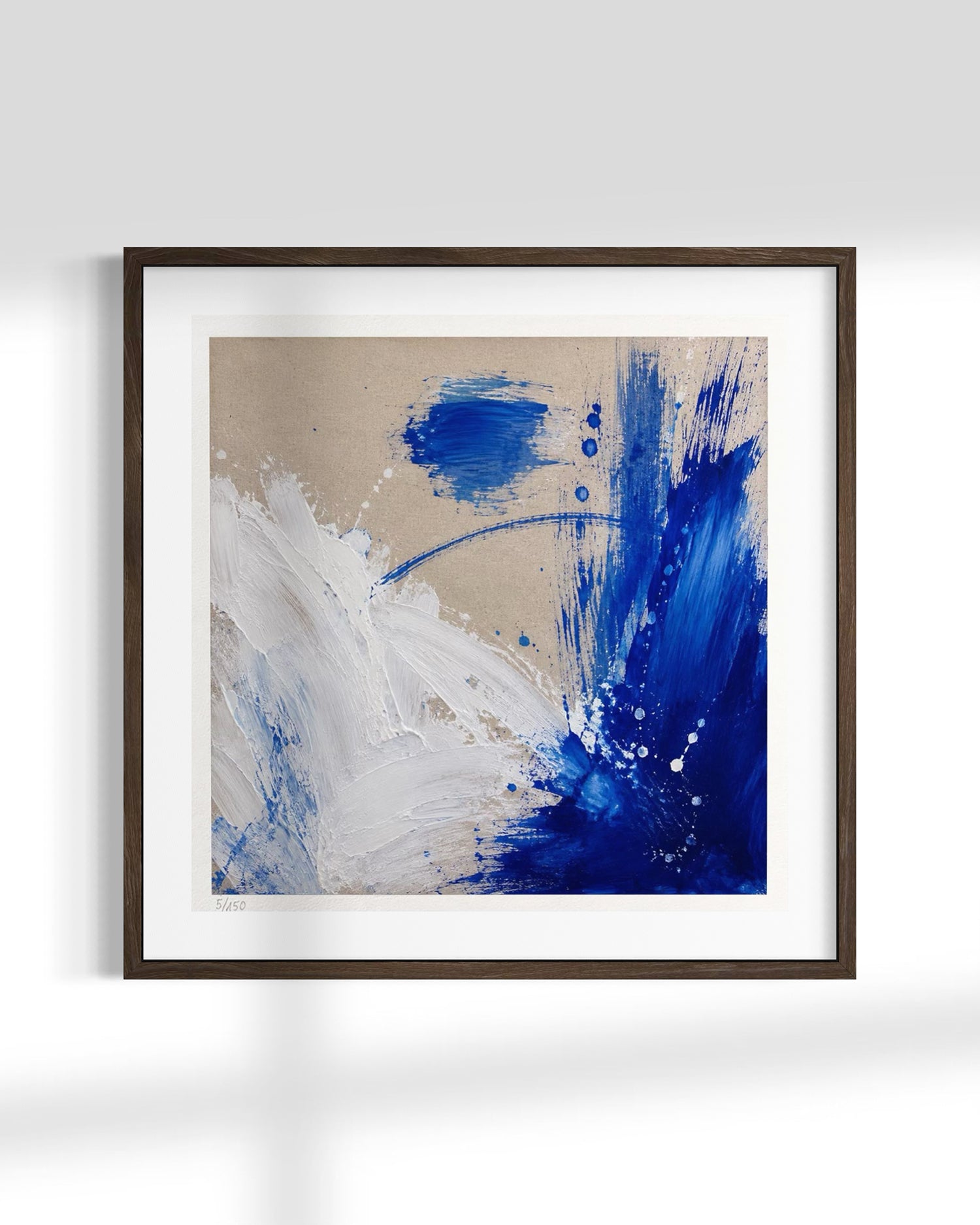 Framed abstract wall art featuring bold blue and white paint strokes on a warm beige background, presented in a dark wood frame with a white mat against a light gray wall.