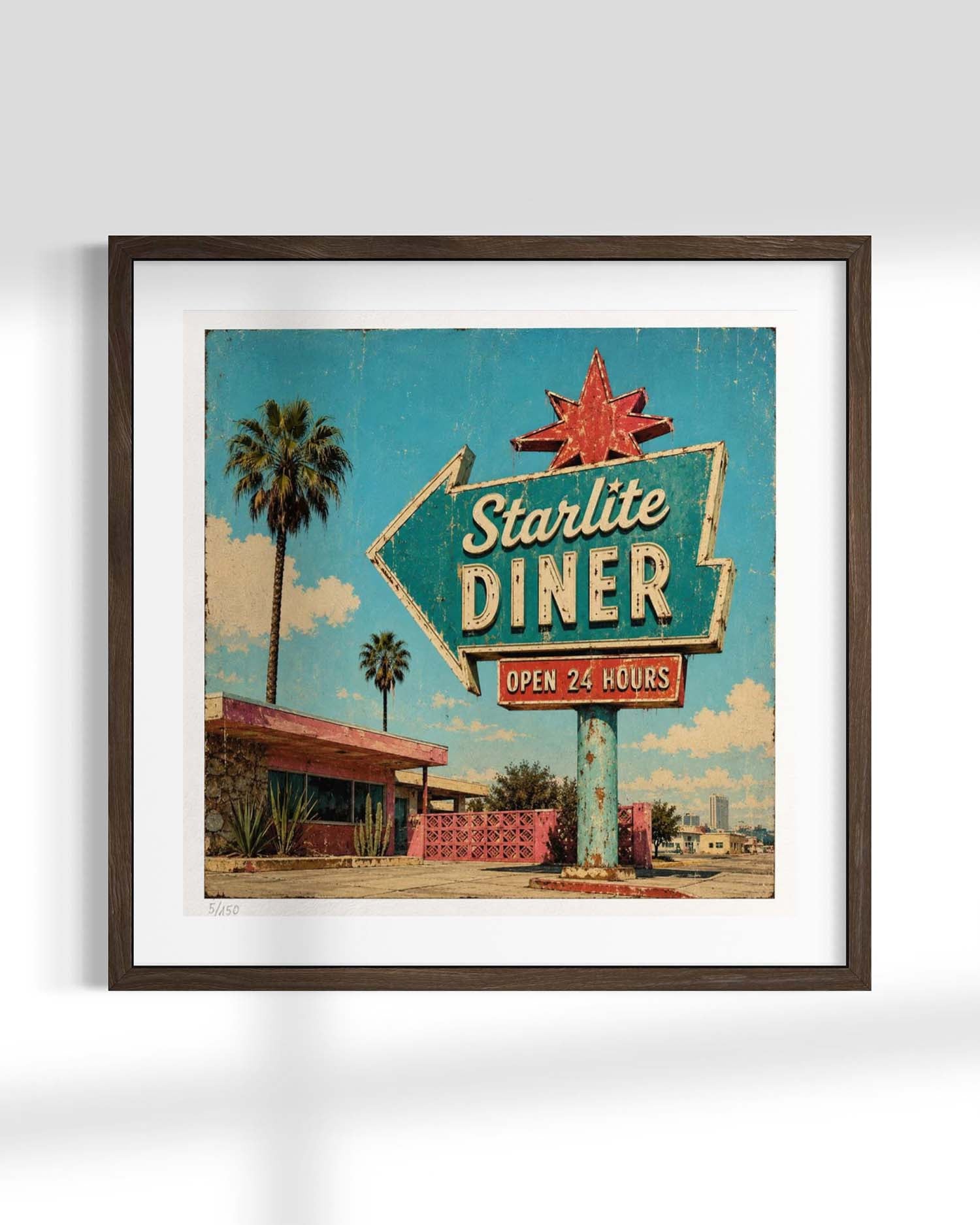 Framed wall art featuring a retro 1950s-style diner sign reading 'Starlite Diner' with palm trees and a blue sky background, shown in a dark wood frame against a light gray wall.