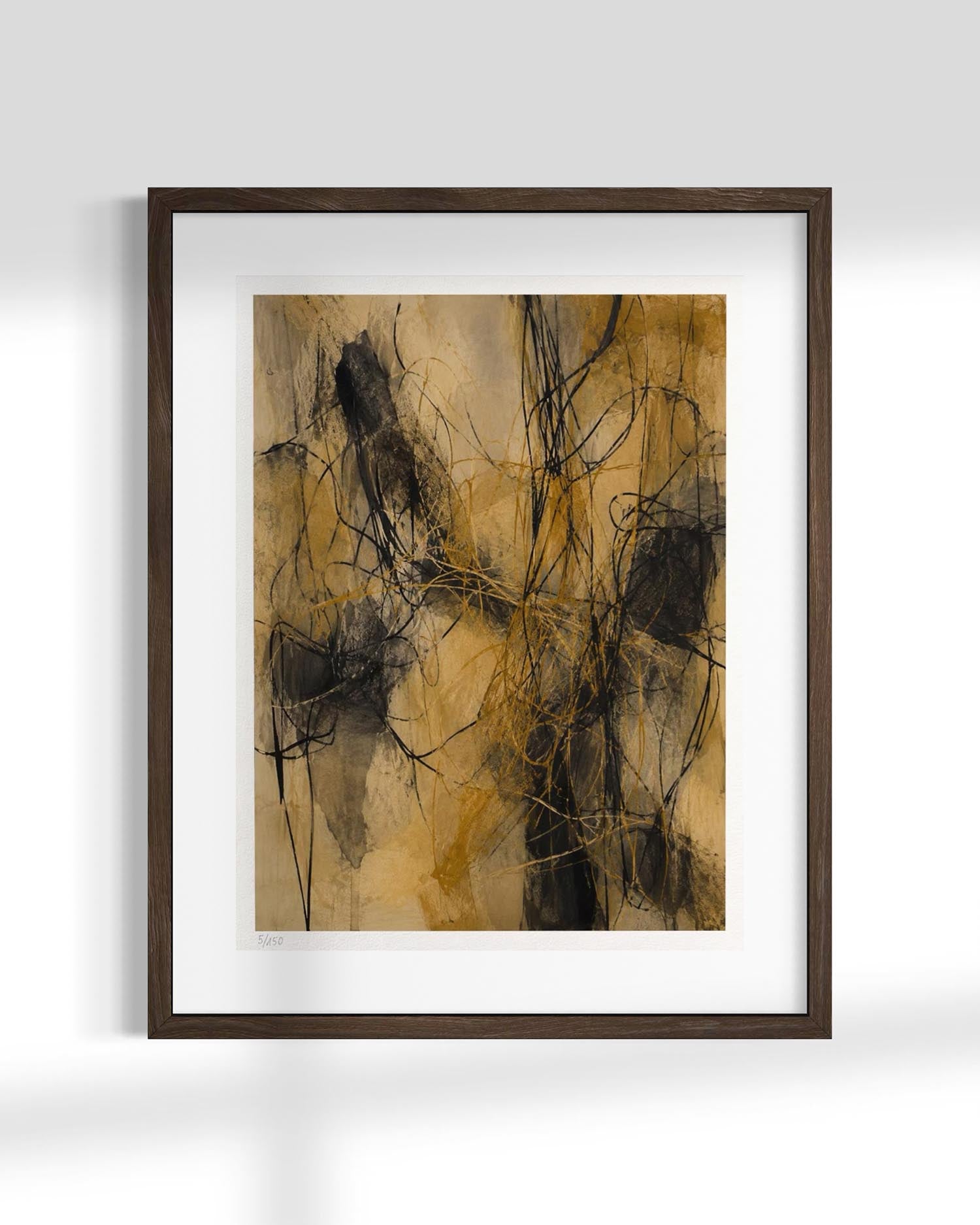 Framed abstract wall art featuring expressive black and dark brown brushstrokes over a warm tan and beige background, displayed in a dark wood frame with a white mat against a light gray wall.