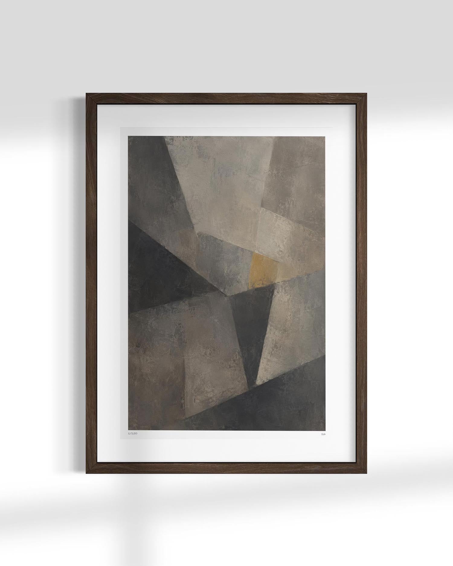 Framed abstract geometric wall art featuring textured gray, black, and taupe shapes with a small warm gold accent, displayed in a dark wood frame with a white mat against a light gray wall.